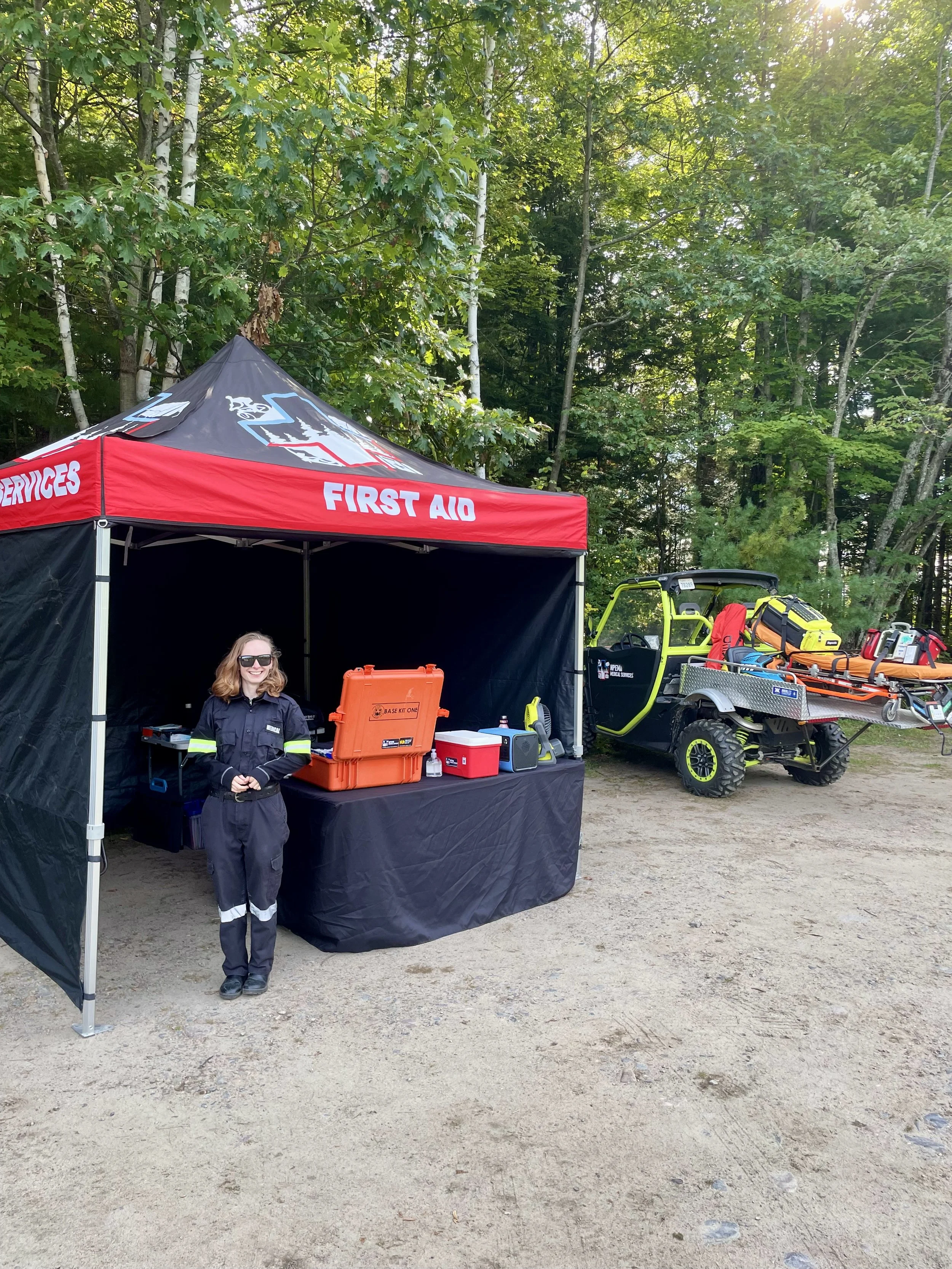 First aid tent with a medical responder, emergency supplies, and an off-road medical vehicle in a wooded area.