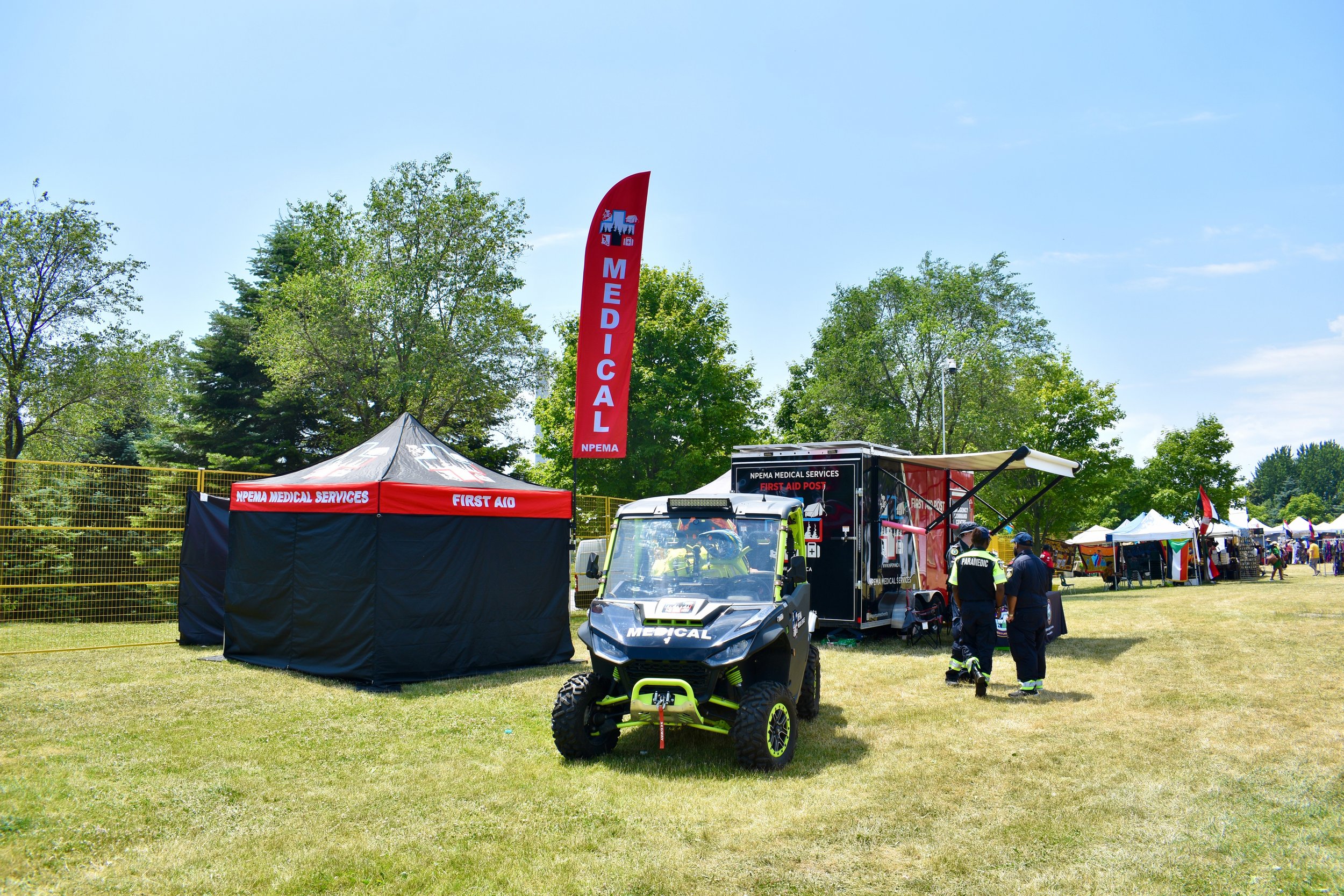 NPEMA Medical Services first aid station with medical tent, utility vehicle, trailer, and paramedics at an outdoor festival.