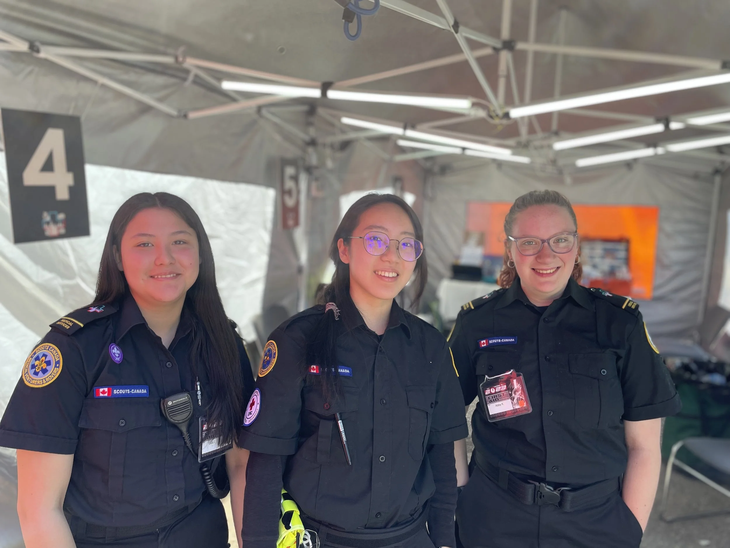 Three Scouts Canada medvent members in uniform pose for a photo inside a medical tent at an event.