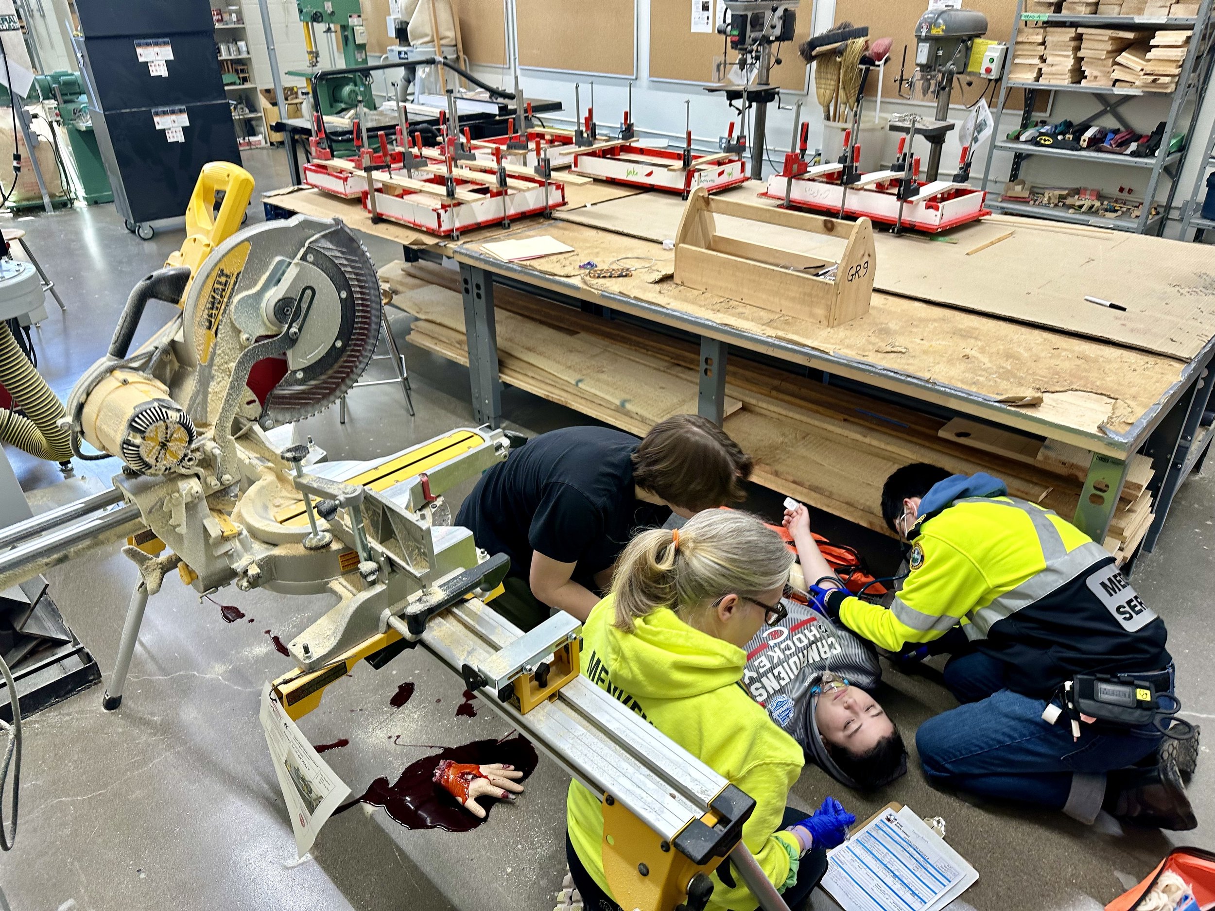 First responders treat an injured person after a workshop accident involving a miter saw in a woodworking shop.
