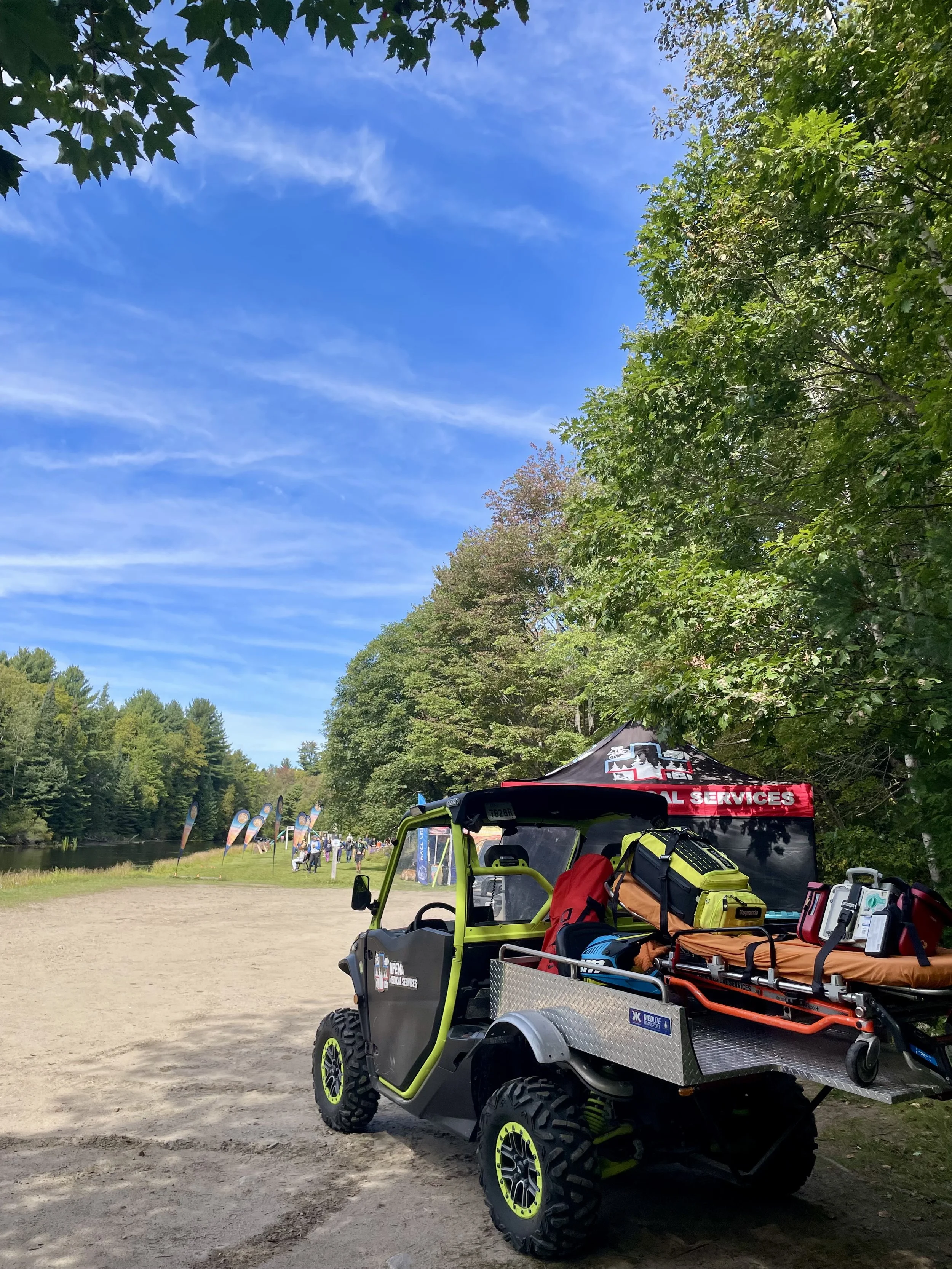 Off-road utility vehicle equipped with emergency medical gear beside a forest lake at an outdoor event