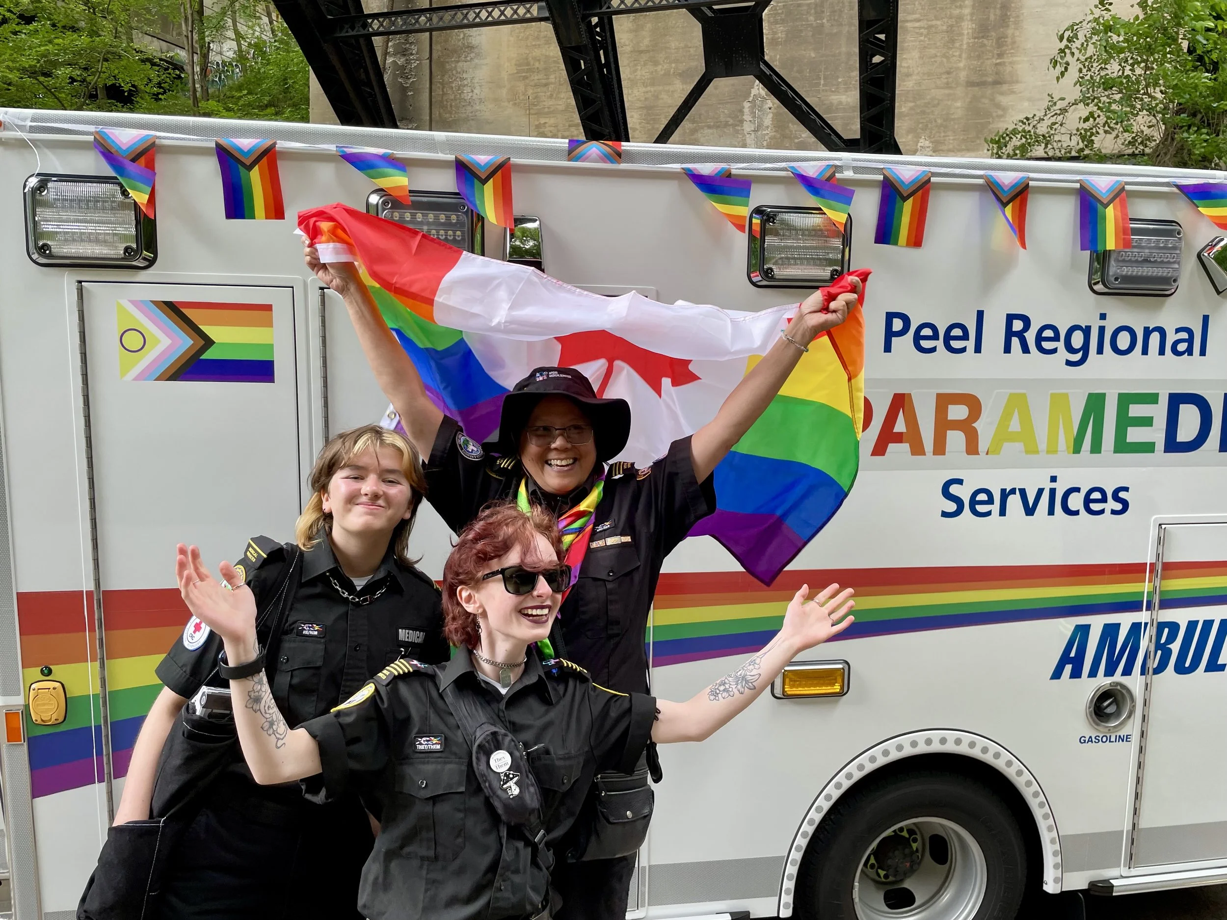 Paramedics pose with Pride flags in front of a Peel Regional Paramedic Services ambulance.