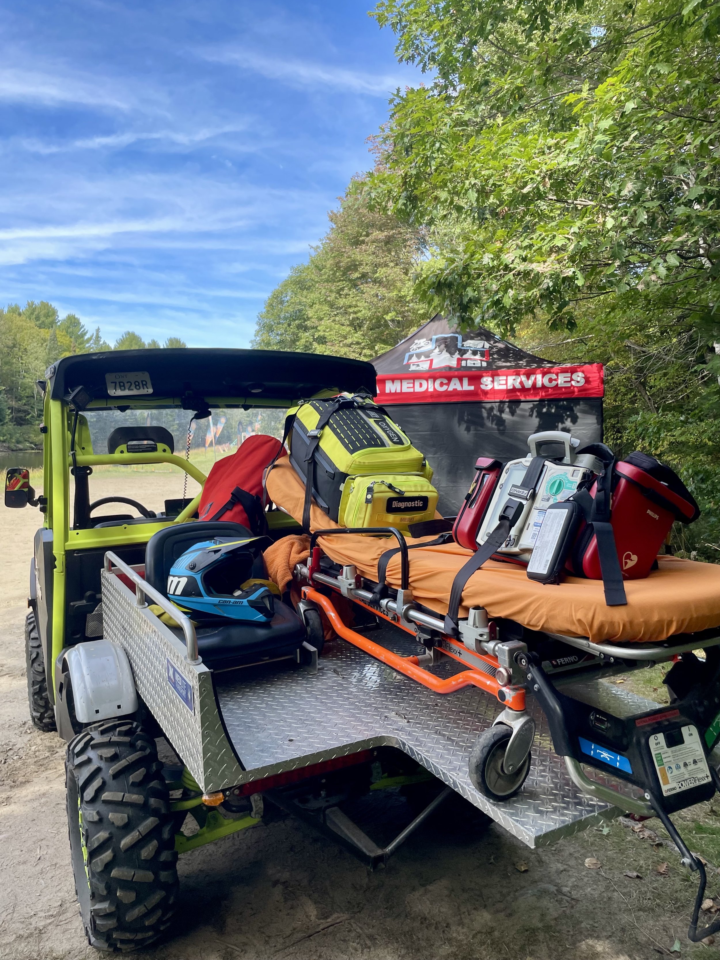 Off-road medical rescue vehicle carrying a stretcher, oxygen bag, defibrillator, and emergency equipment on a wooded trail.
