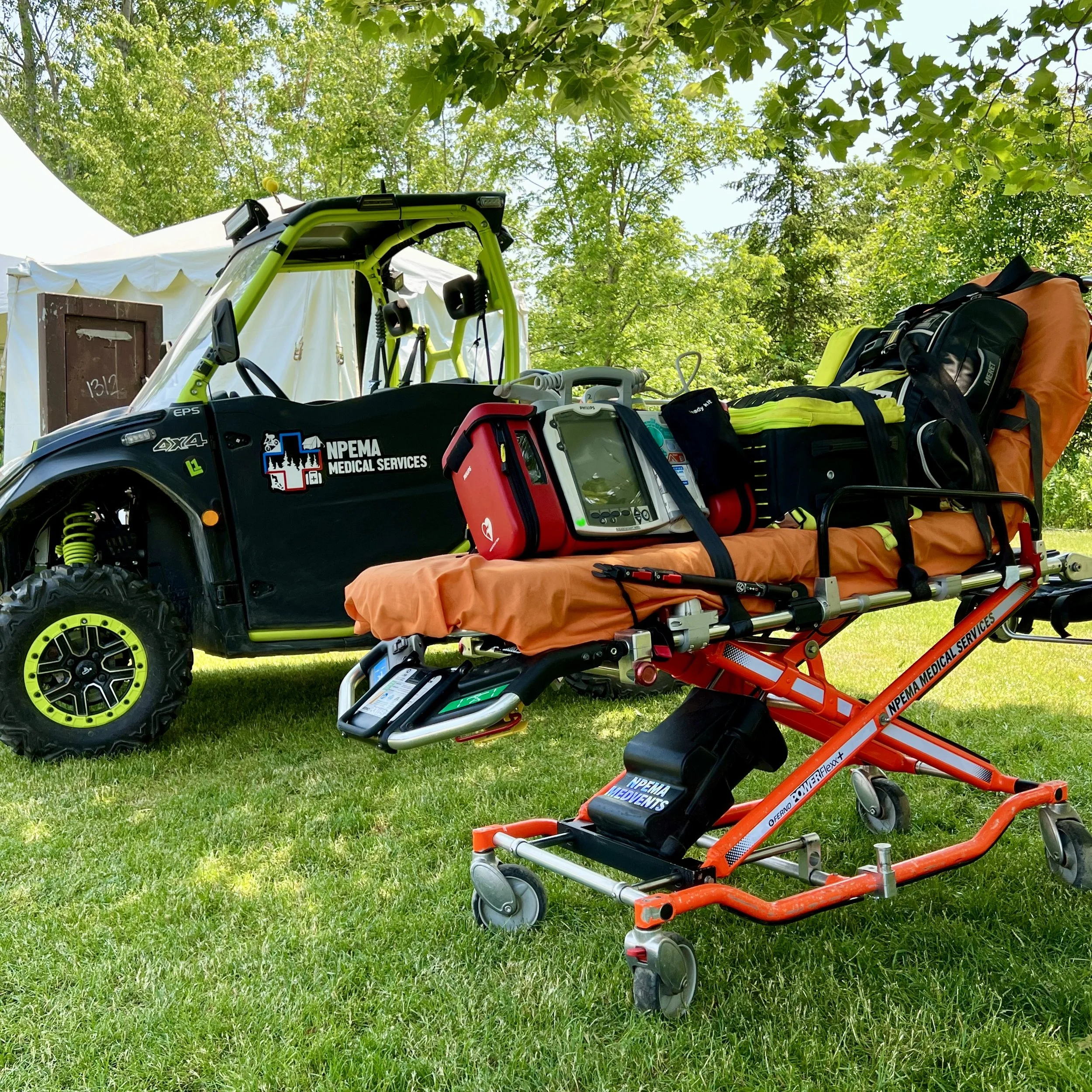 NPEMA Medical Services off-road utility vehicle loaded with emergency medical equipment, stretcher, and rescue gear on grass outside a tent