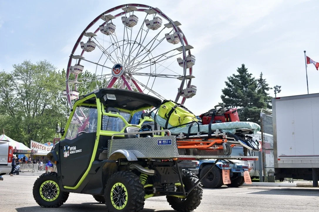 Utility vehicle carrying emergency rescue equipment in front of a Ferris wheel at a fairground