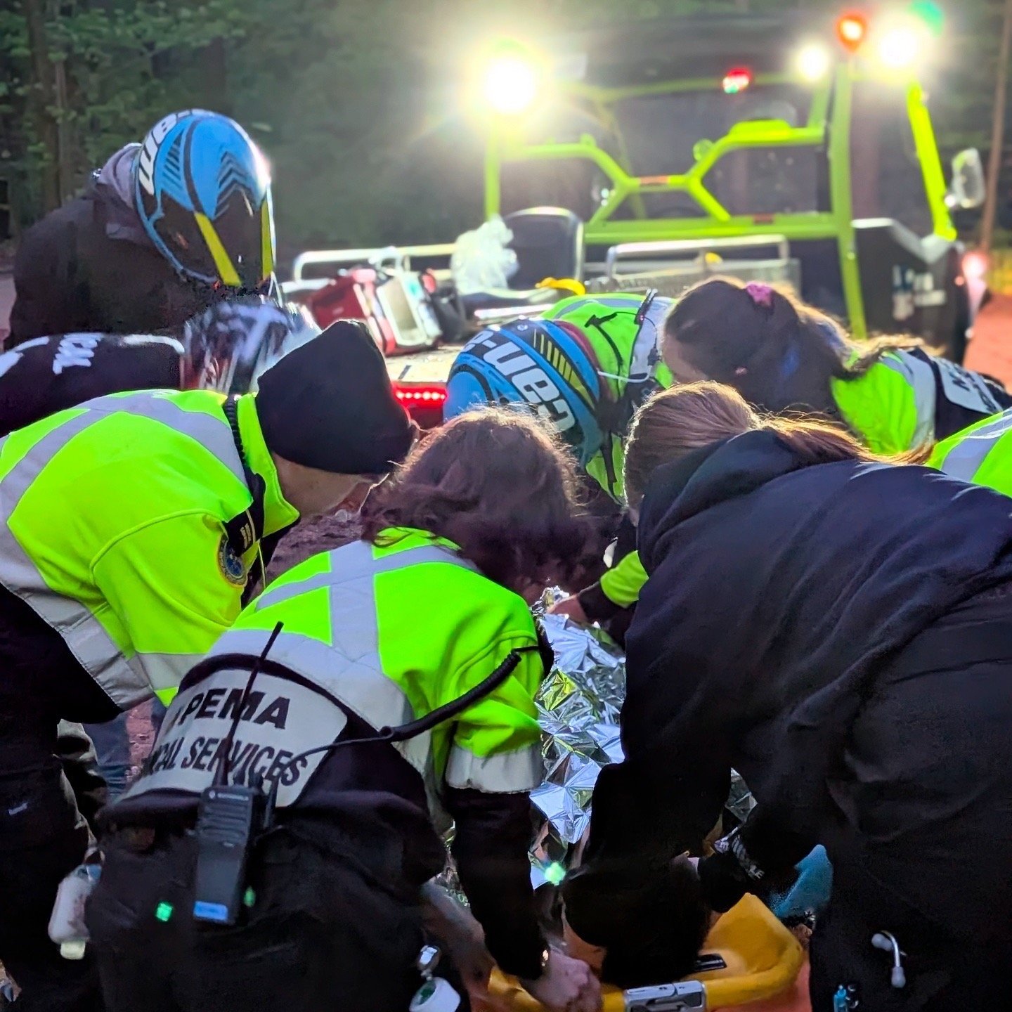 Emergency responders in high-visibility jackets provide medical aid beside an ambulance at night.