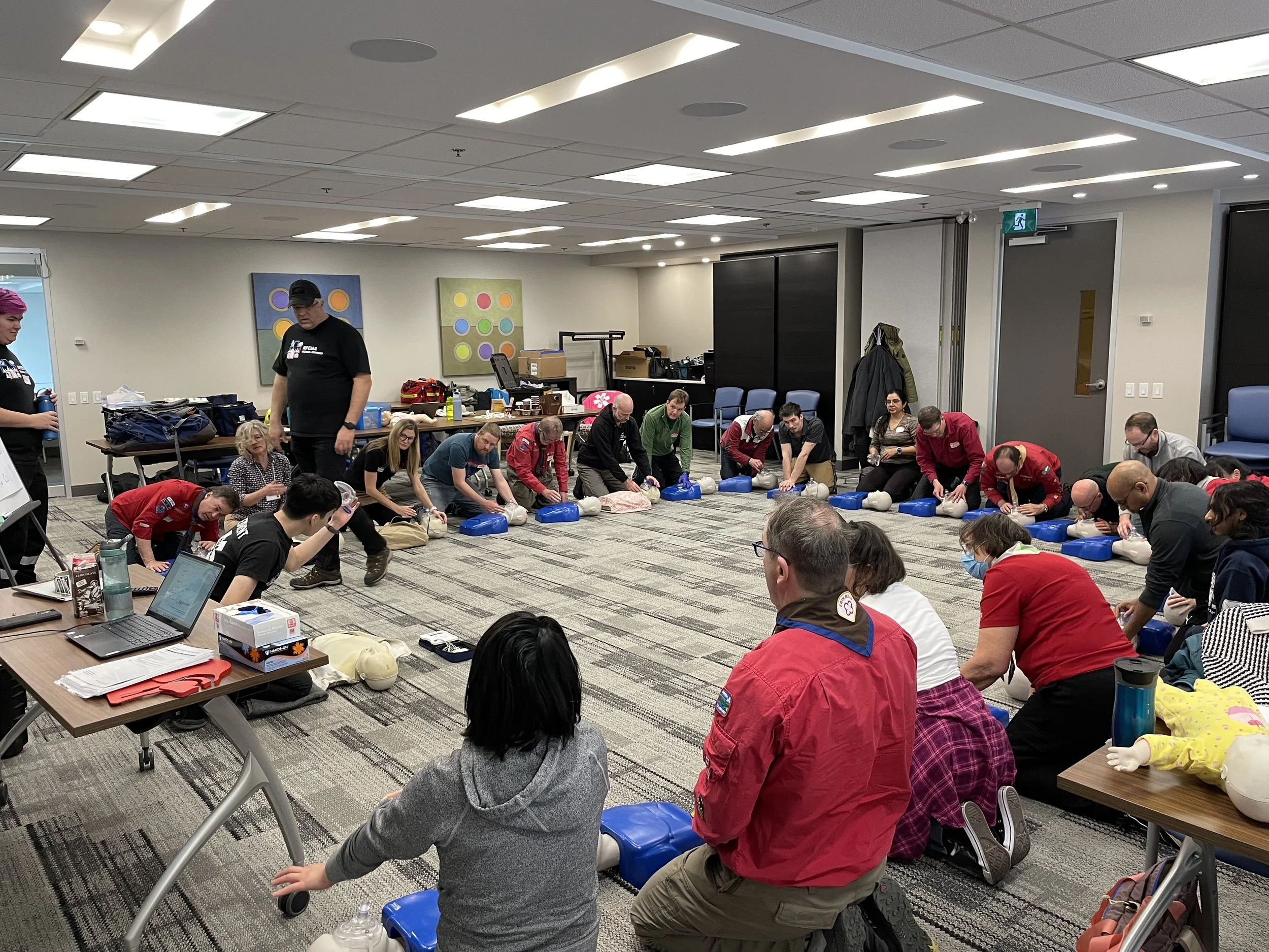 First aid training class practicing CPR on mannequins in an office conference room