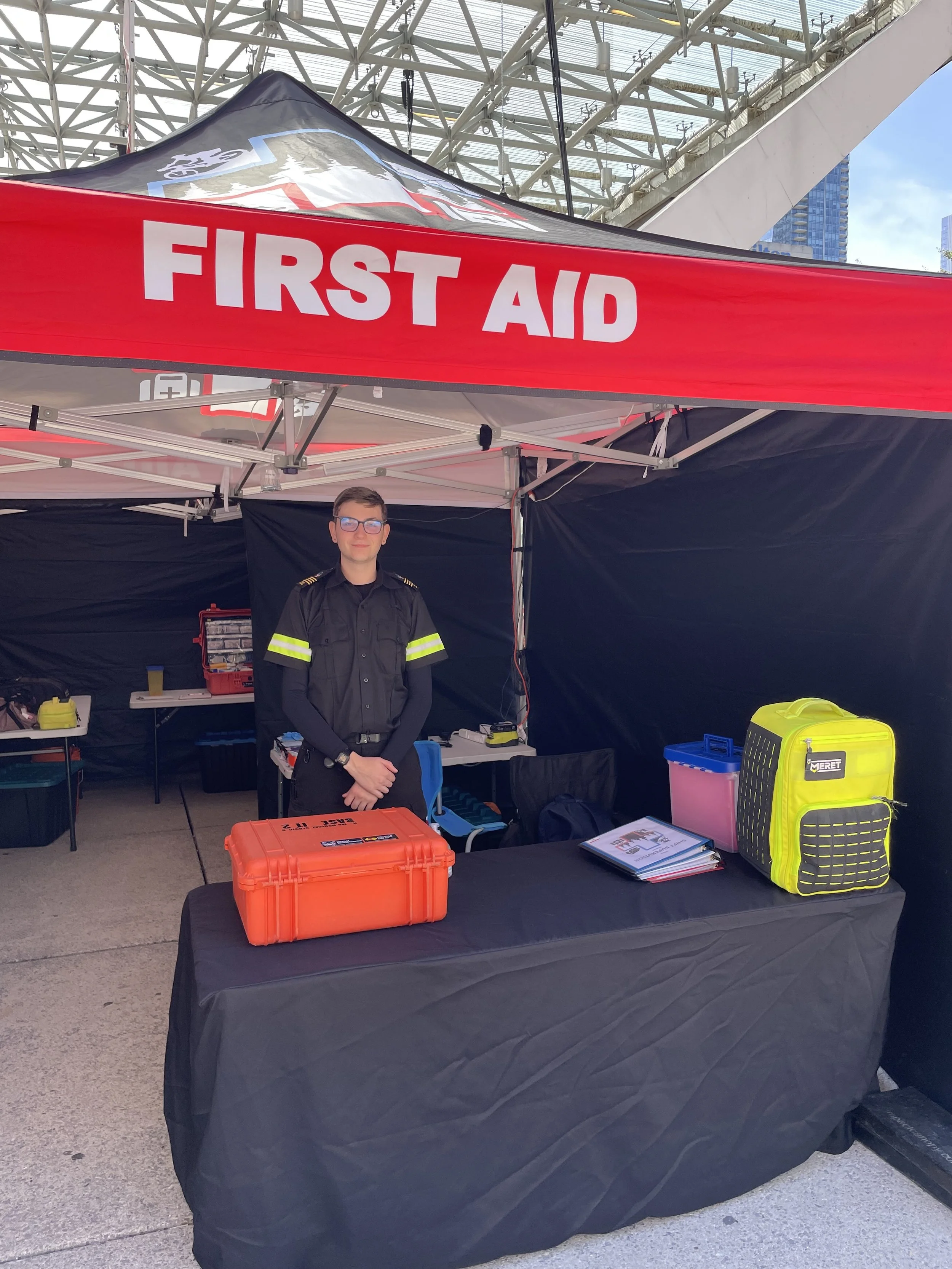 First Aid booth with a uniformed responder, medical equipment, and a large red “FIRST AID” sign at an outdoor event