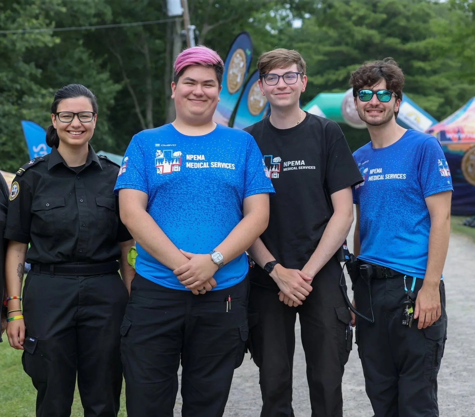 Four smiling NPEMA Medical Services team members pose outdoors at an event.