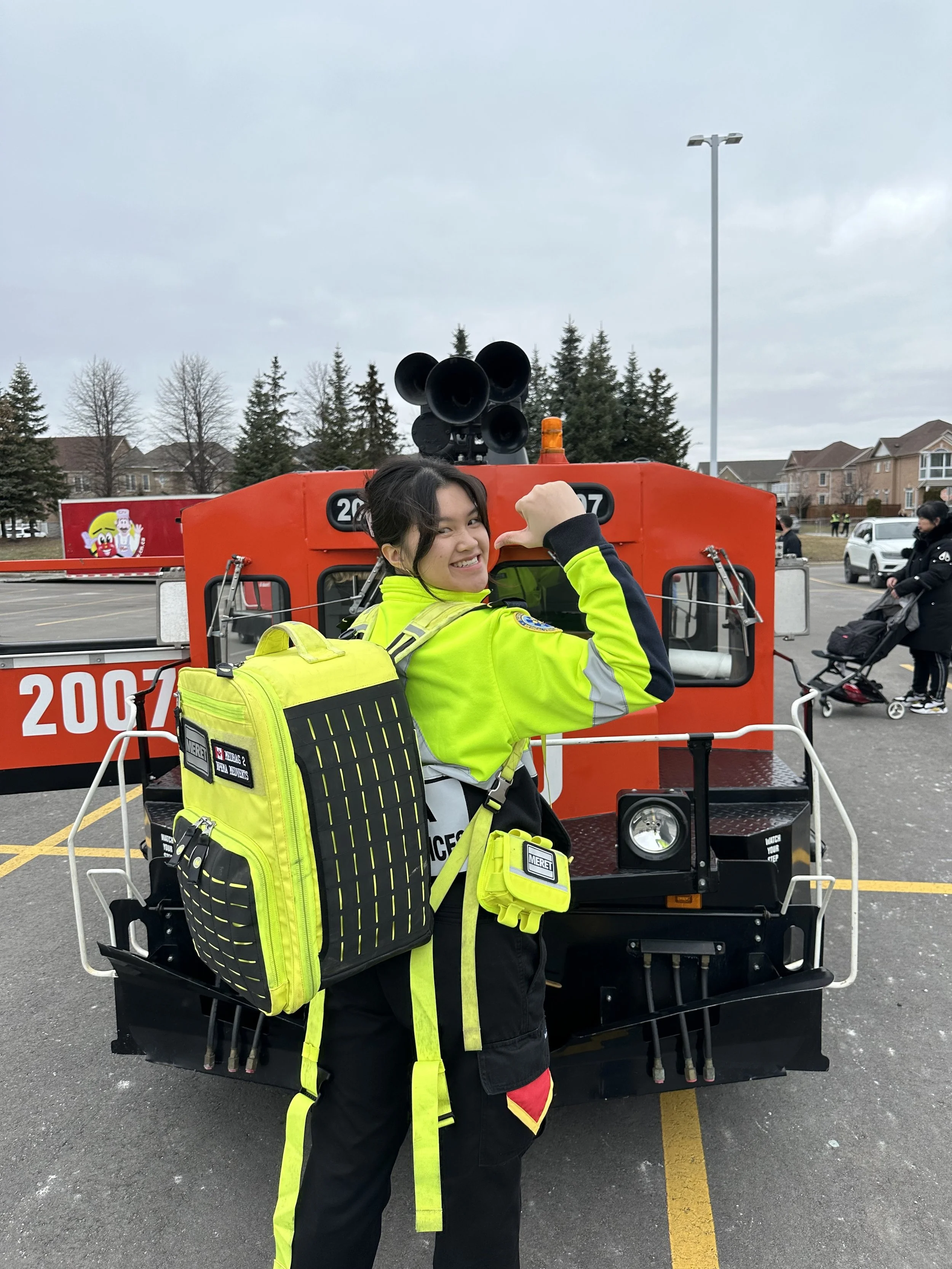 Emergency responder in a neon yellow uniform posing in front of a red fire truck with siren horns.