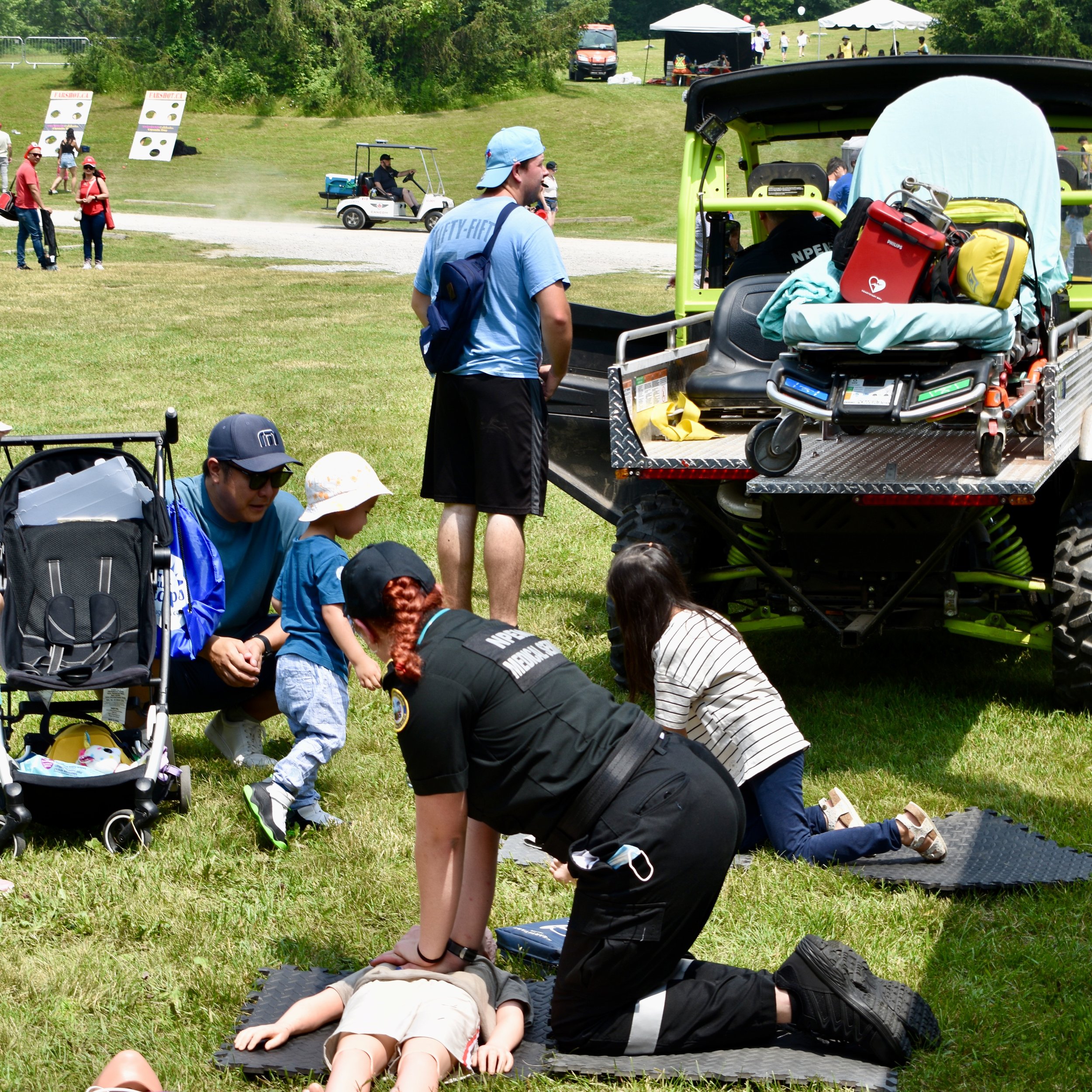First responders perform a mock rescue beside an all-terrain utility vehicle at an outdoor community event.