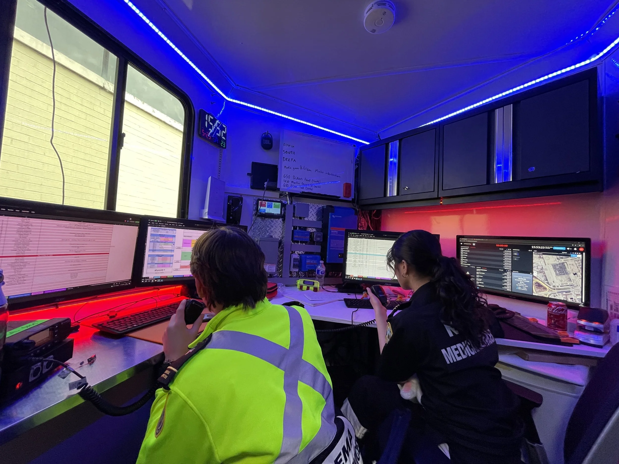 Emergency dispatch trailer and control room with two operators monitoring multiple computer screens under blue and red LED lighting