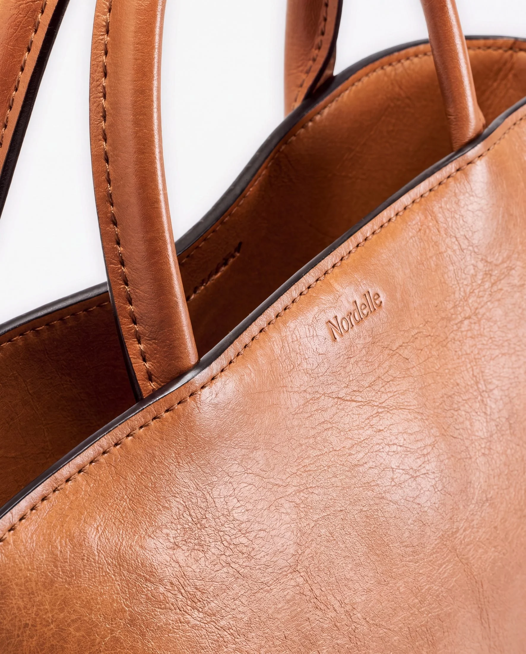 Close-up of a tan leather handbag with stitched handles and embossed text.