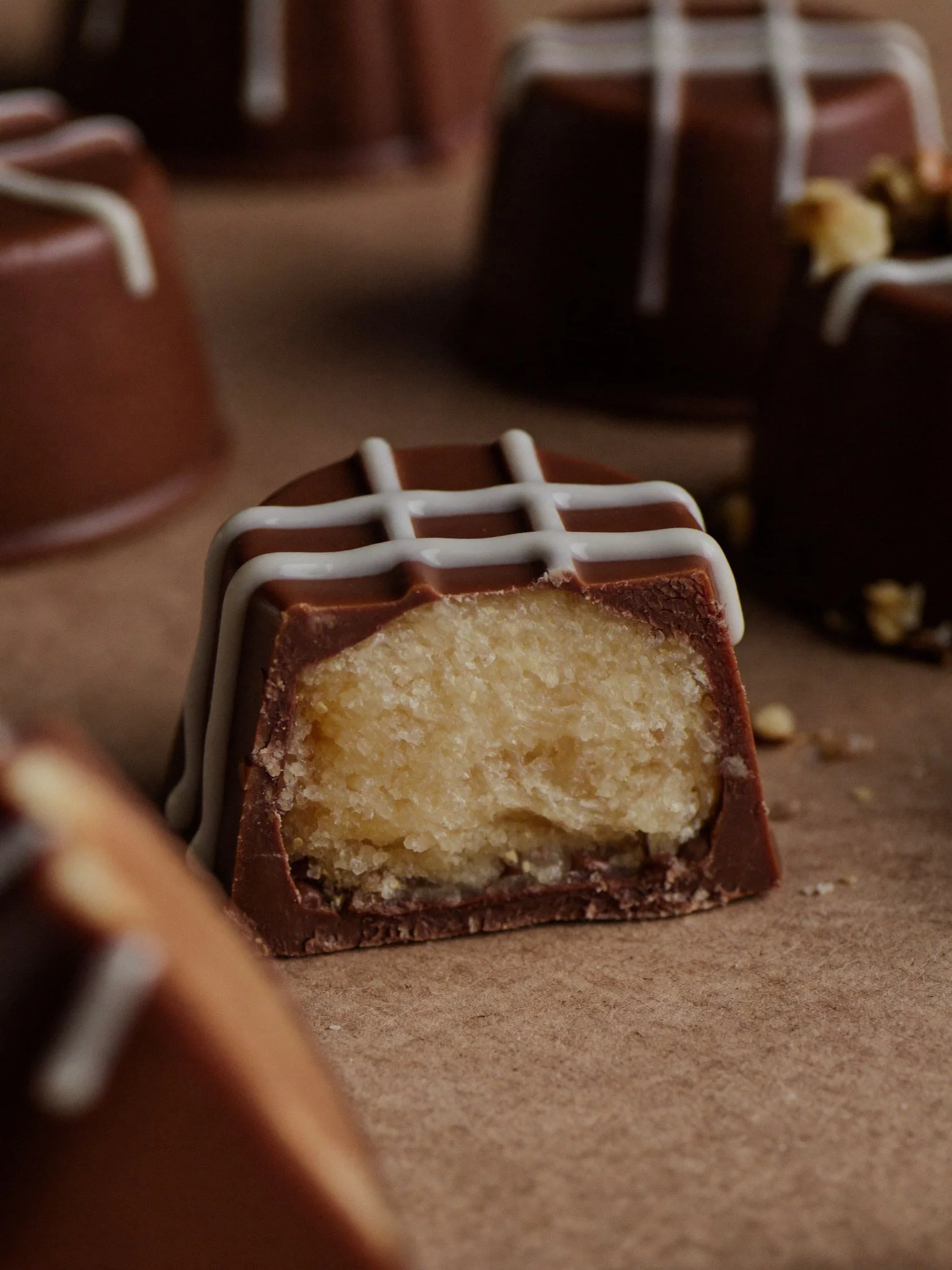 Close-up of a partially eaten chocolate-covered candy with a coconut filling, placed on brown paper, with other candies blurred in the background.