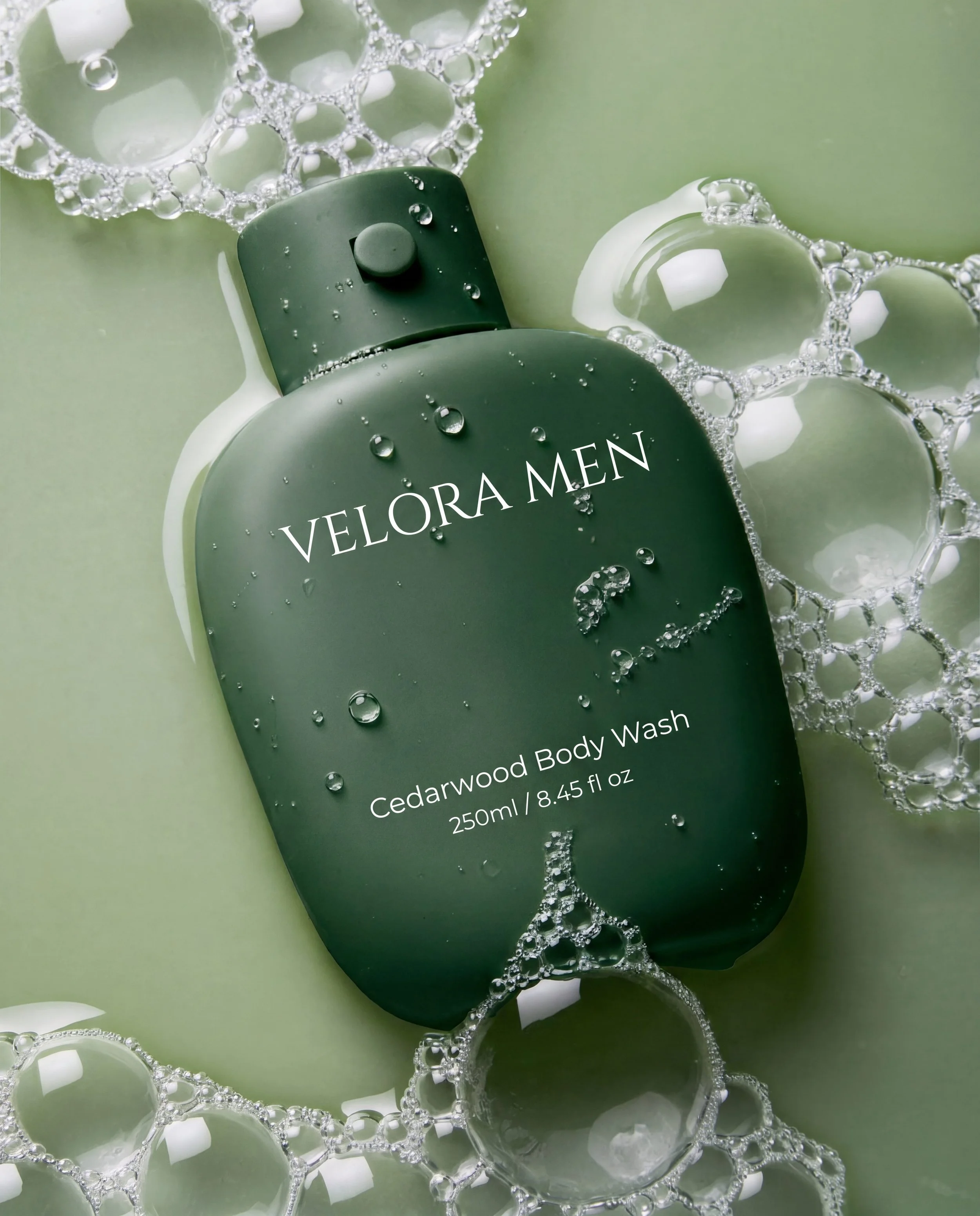 Close-up of a velora men cedarwood body wash bottle with water droplets and bubbles on a green background.