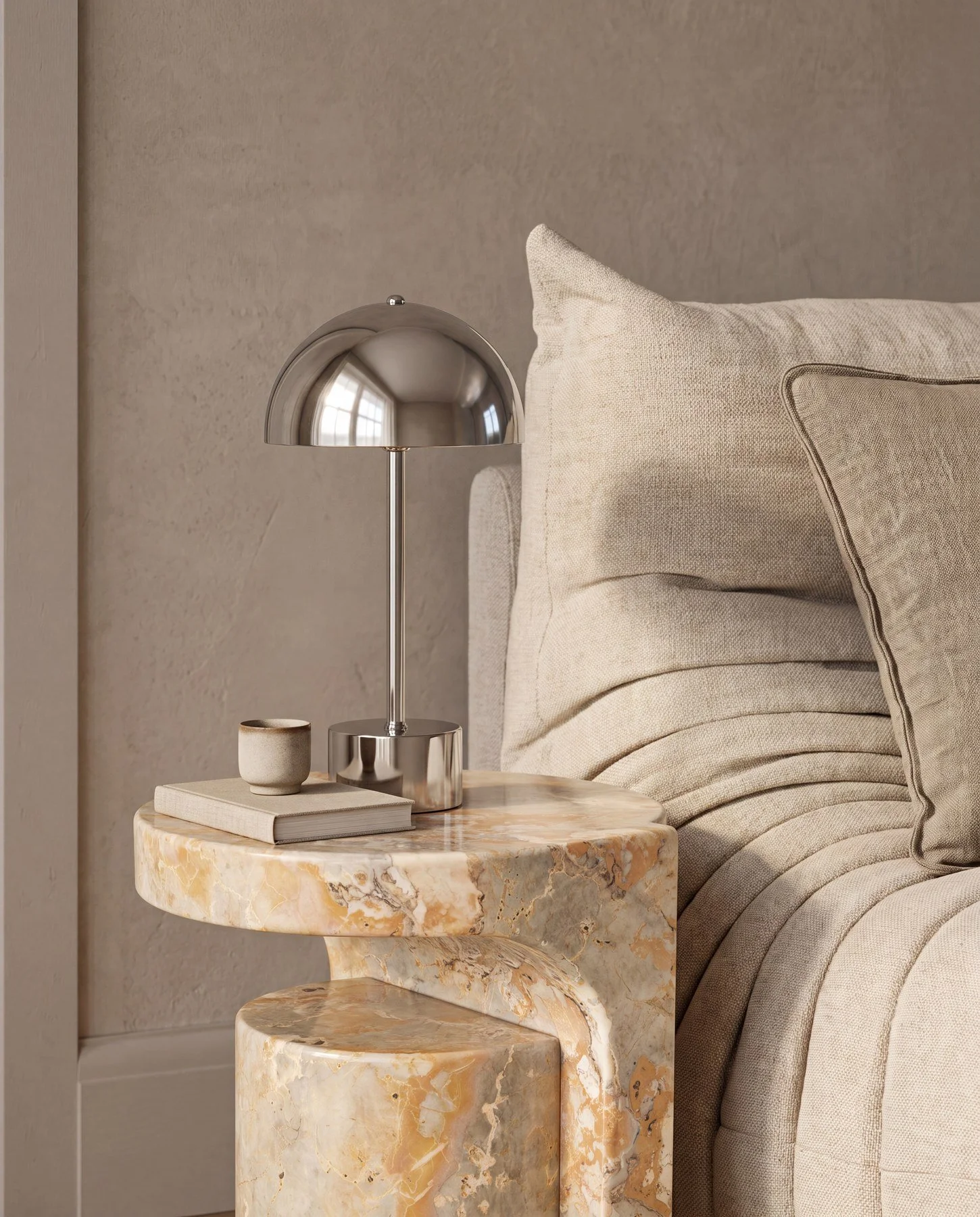 A close-up of a beige textured sofa with a decorative pillow, a gold-colored marble side table, and a modern chrome desk lamp with a round base and semi-circular shade, accompanied by a small beige cup and a closed book on the table.