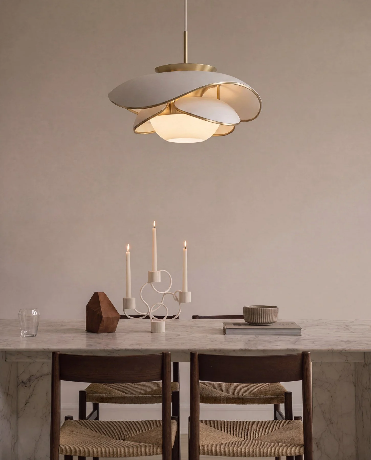 Dining room table with candles, bowl, and decorative objects, illuminated by modern ceiling pendant light.