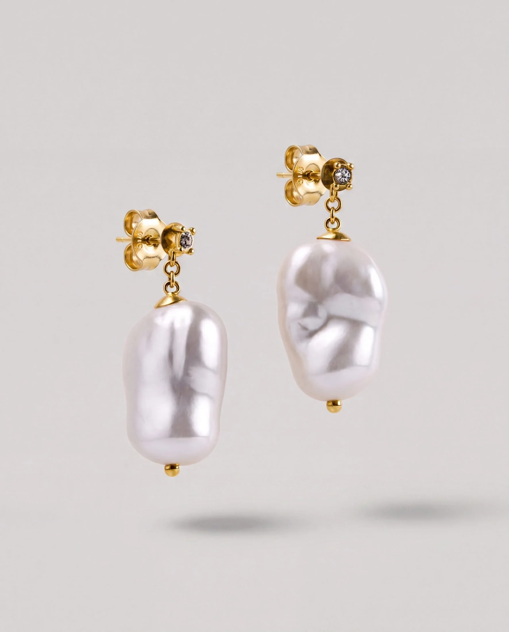 Close-up of gold earrings with pearls and small diamonds, positioned on a white display.