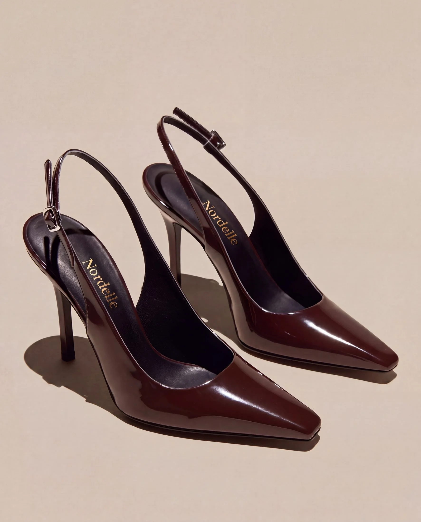 A set of three men's high-heeled shoes in dark red patent leather with pointed toes and an ankle strap, viewed against a plain beige background.
