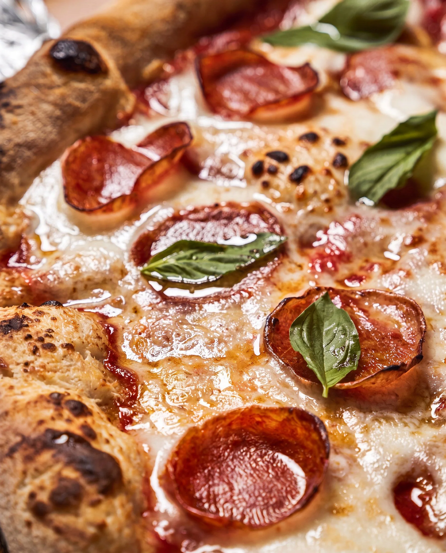 Close-up of a pizza with pepperoni slices, basil leaves, and melted cheese.