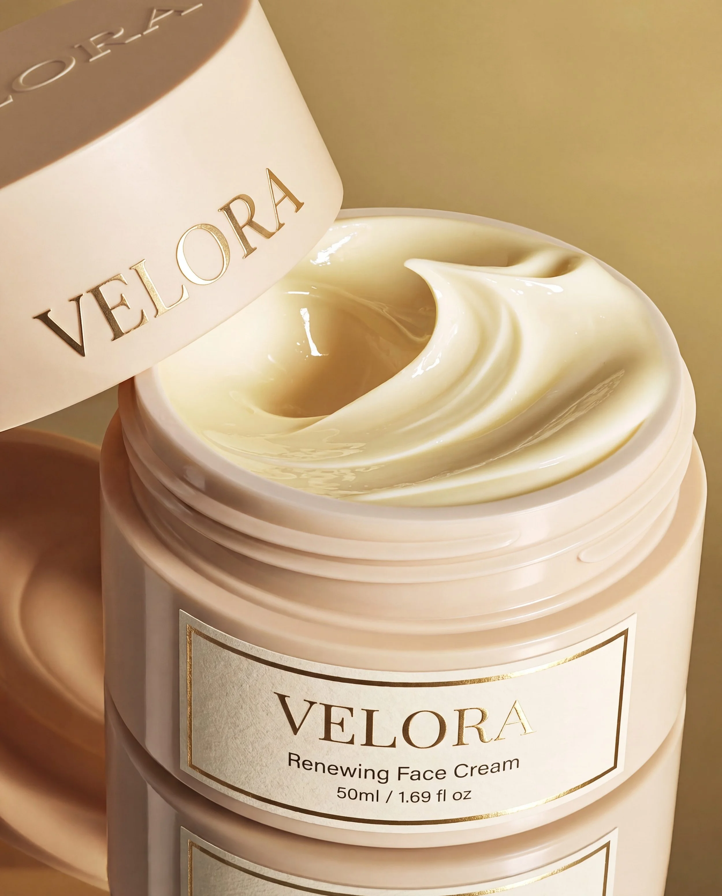 A jar of Velora renewing face cream with the lid slightly open, showing the creamy texture inside. The label on the jar and the lid are visible, with the message 'Velora' and the description 'Renewing Face Cream, 50ml / 1.69 fl oz'.