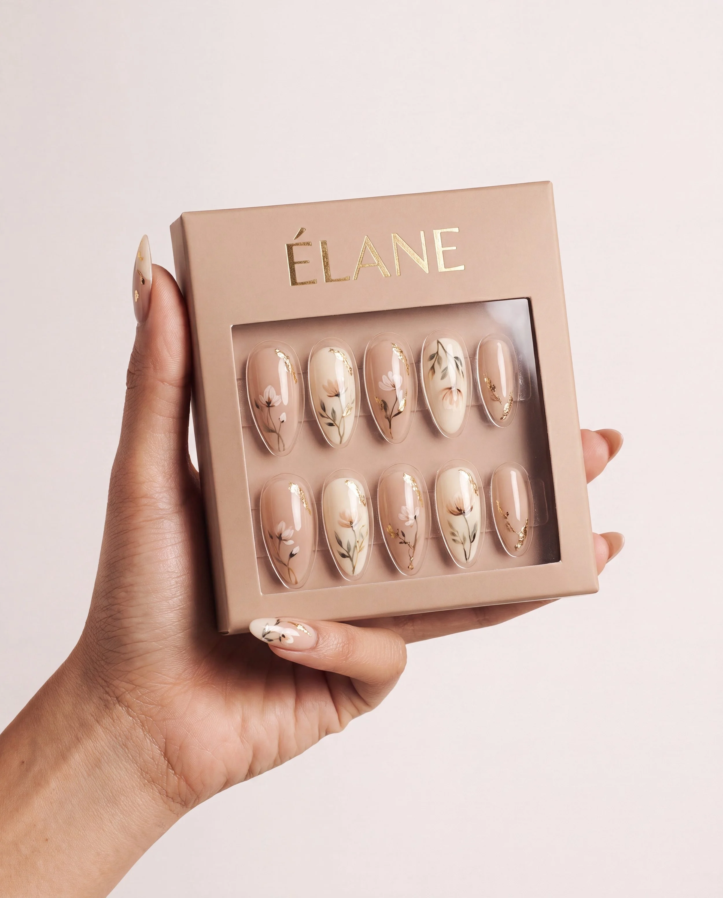 Hand holding a box of decorated fake nails with floral and gold designs, with brand name 'ÉLANE' on the box.