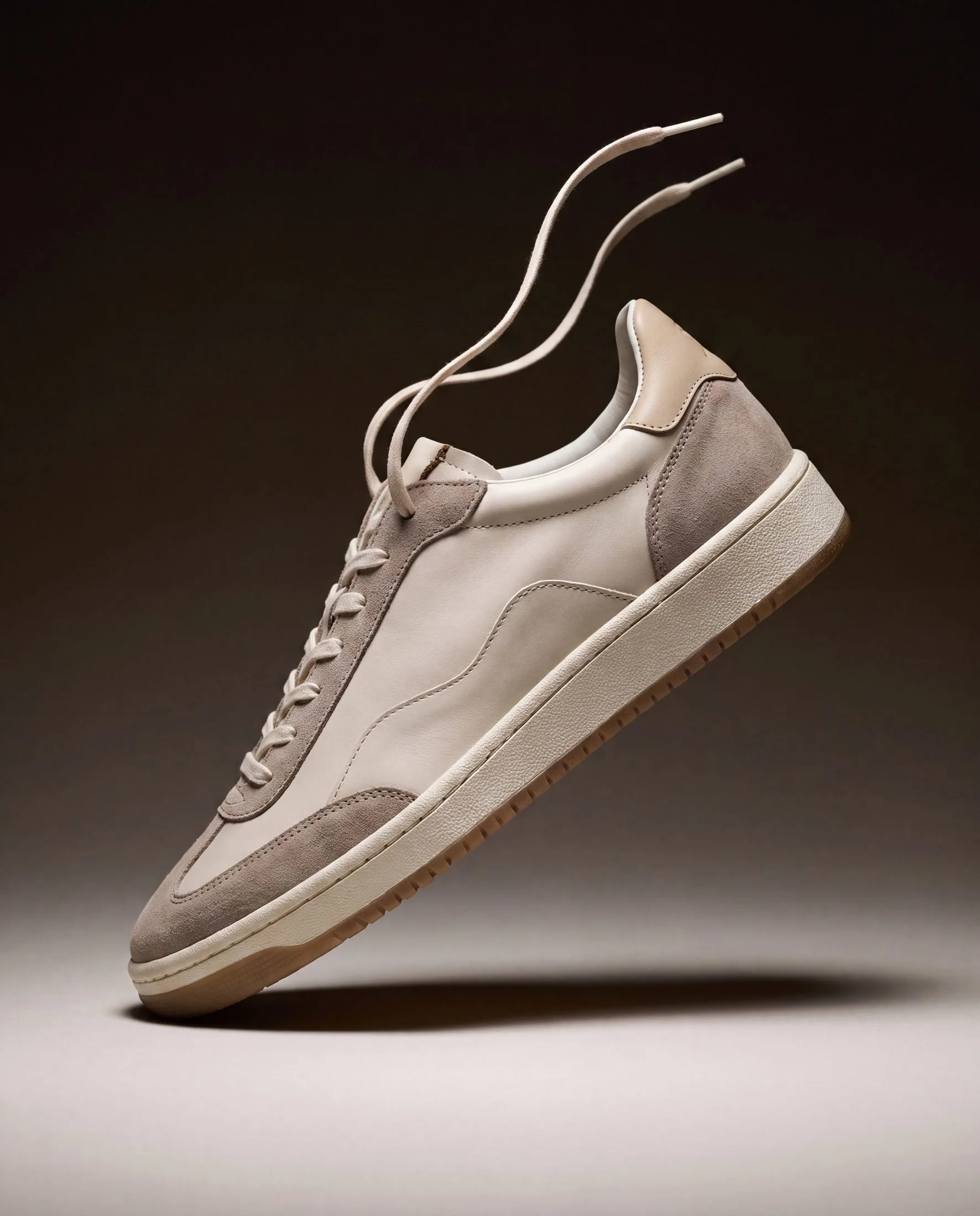 A beige and gray sneaker suspended in mid-air against a dark background.
