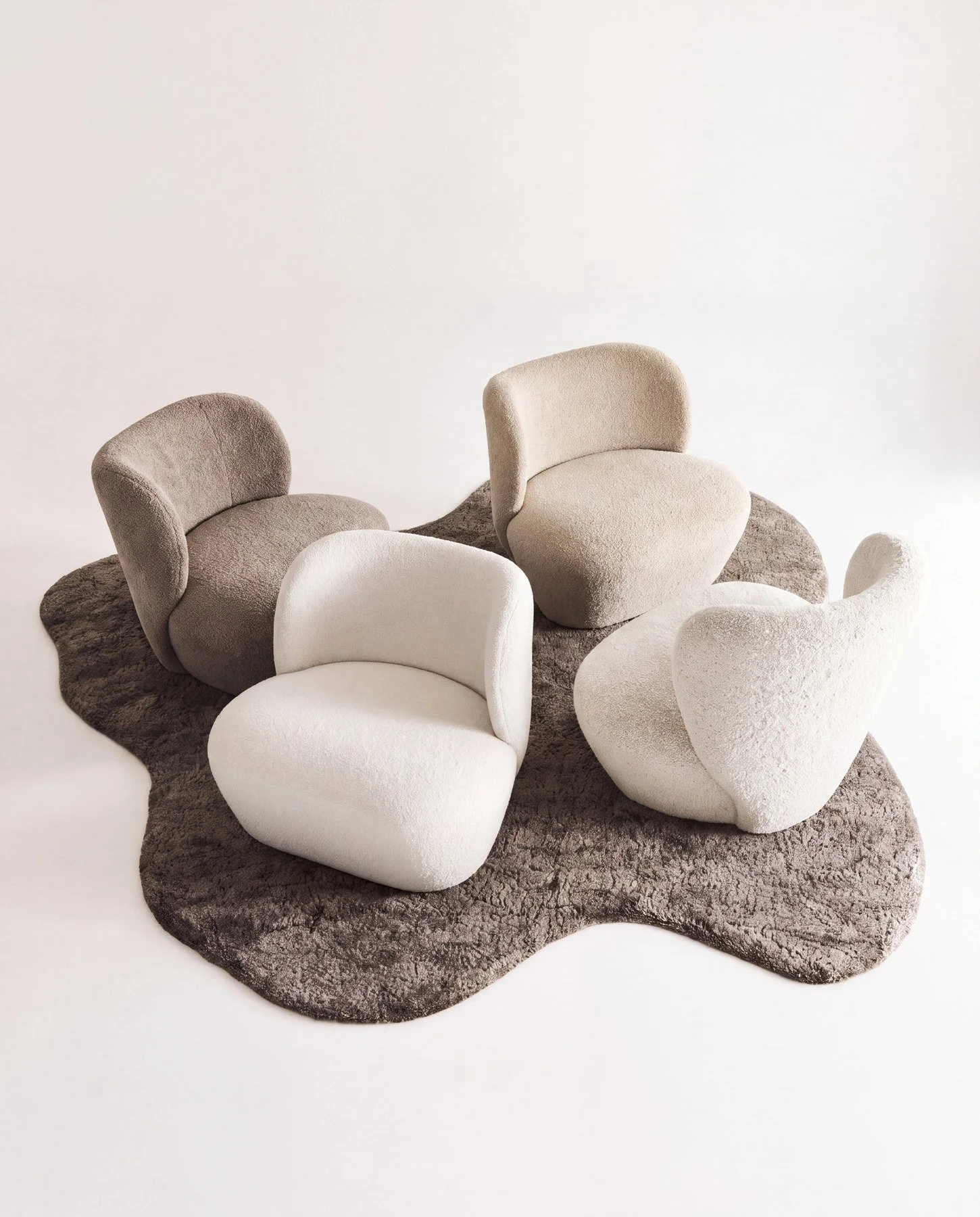 Modern plush chairs in neutral tones arranged on a textured rug against a plain white background.