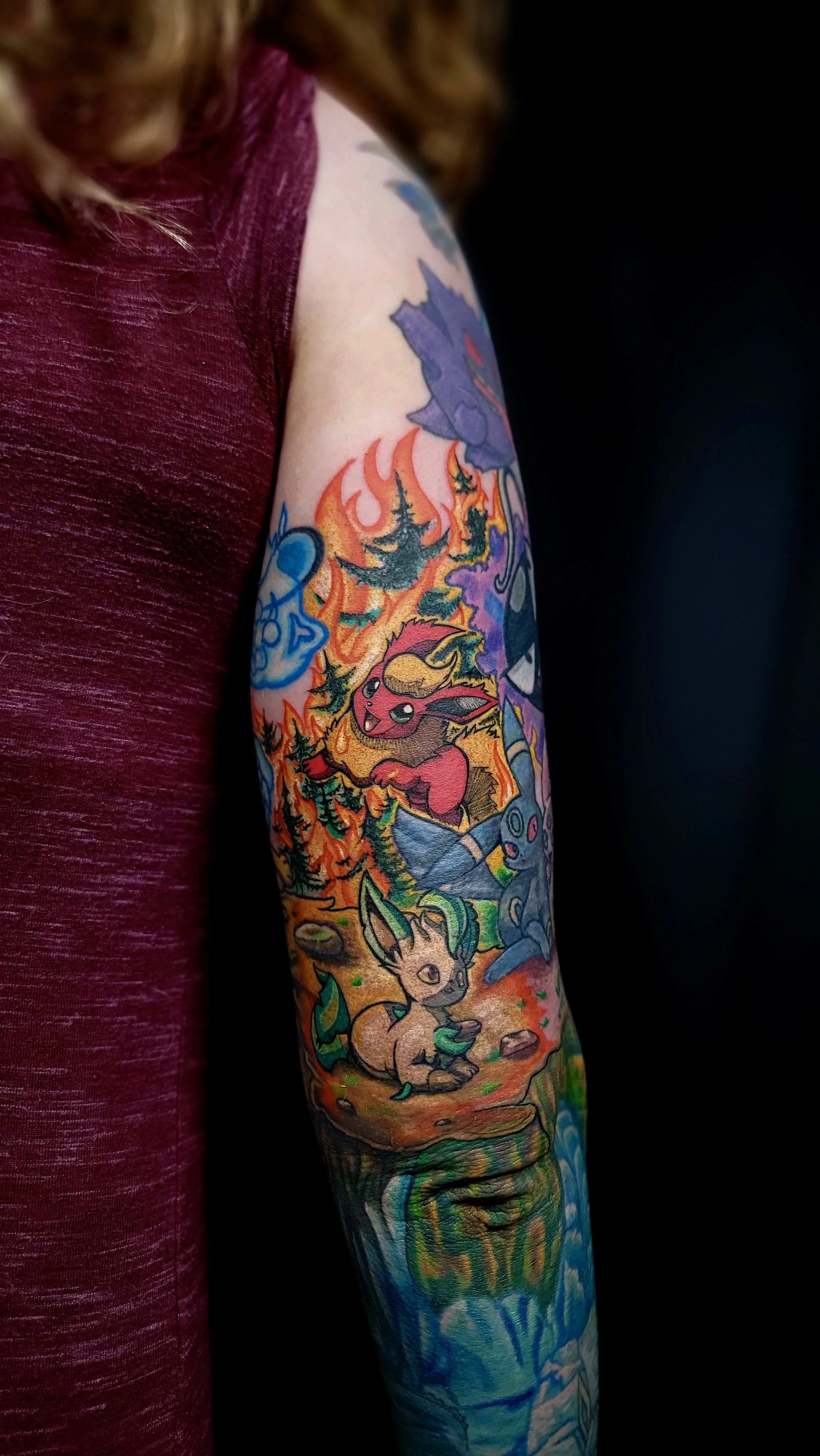 Colorful tattoo sleeve featuring Pokémon characters, including Pikachu, Eevee, and others, with vibrant flames and nature elements.