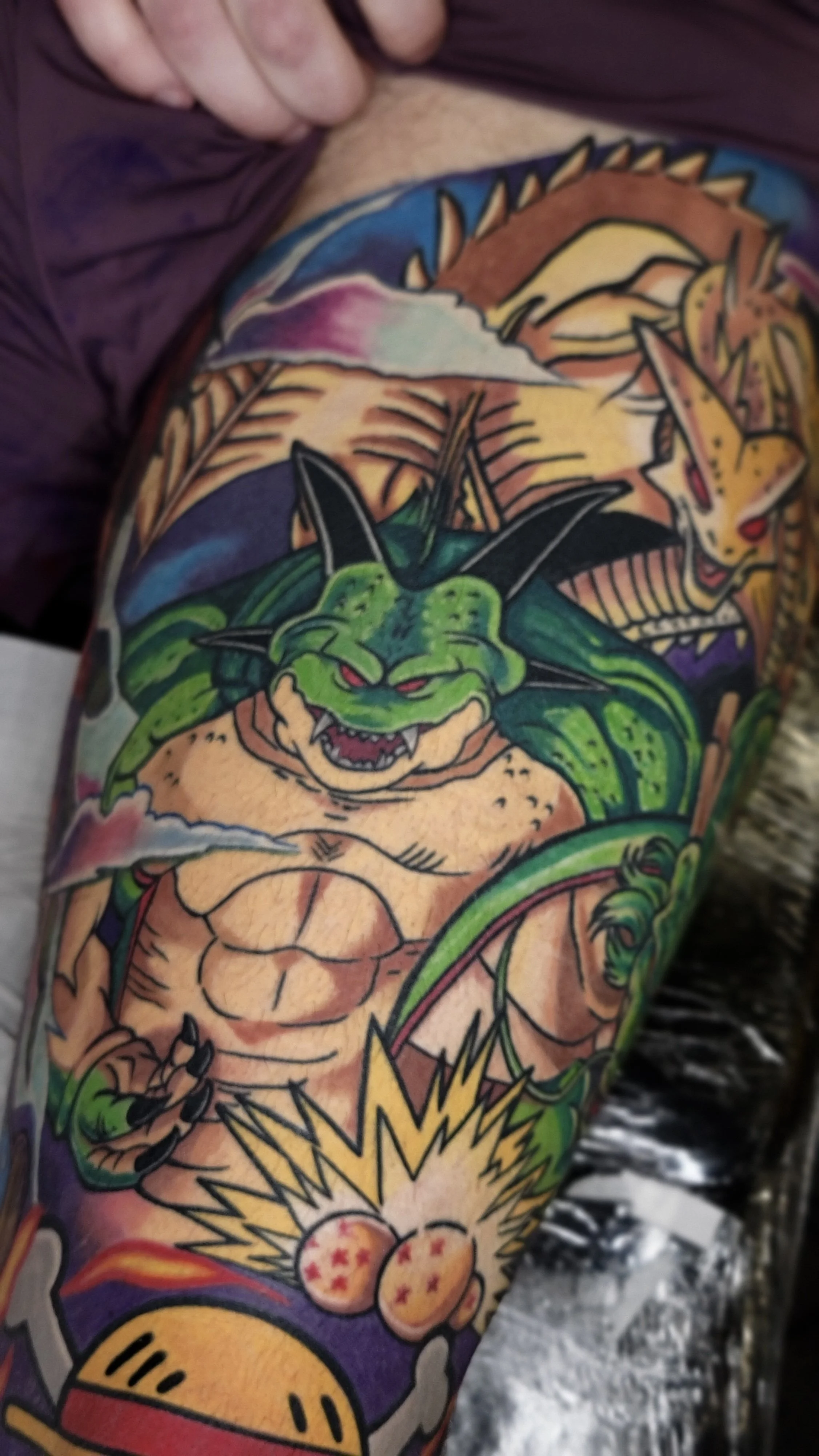 Colorful tattoo sleeve featuring a green dragon with red eyes and sharp teeth, a roaring tiger, and various other vibrant mythical and fantasy elements.