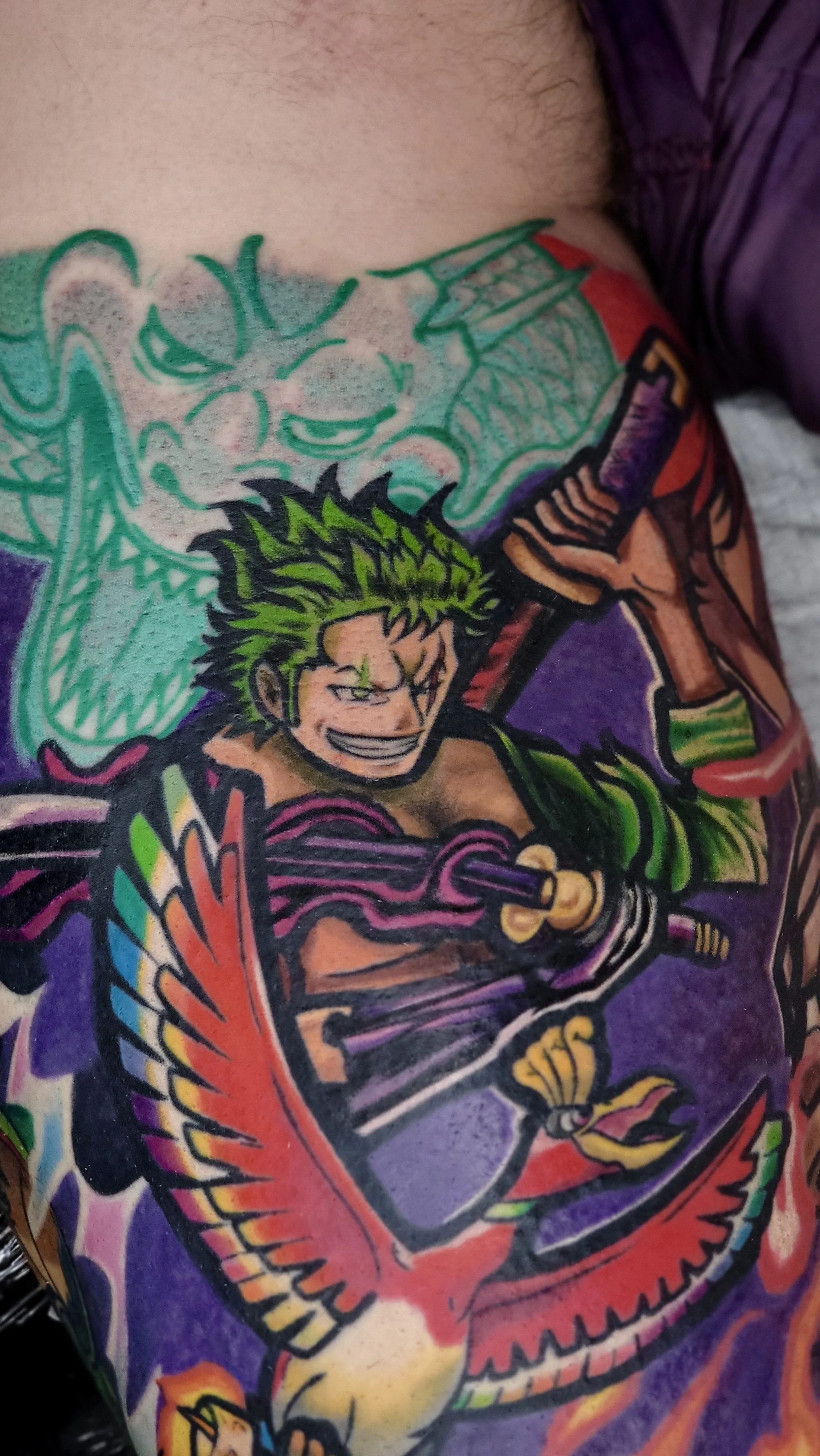 Colorful tattoo of a young man with spiked hair wielding a sword, with a dragon design in the background.