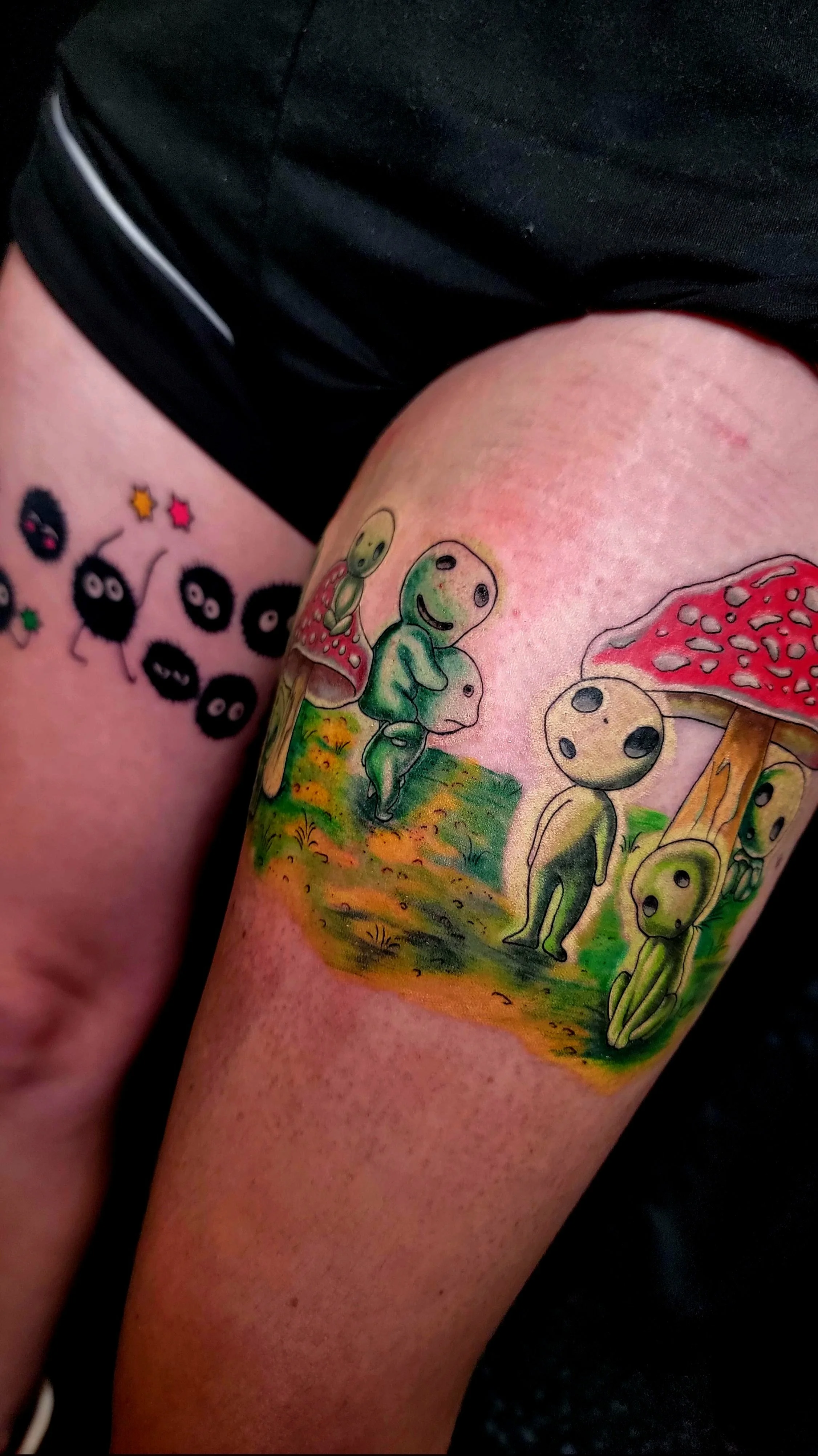 Colorful tattoo of cartoon-like characters with mushroom hats and rounded features on a person's arm.