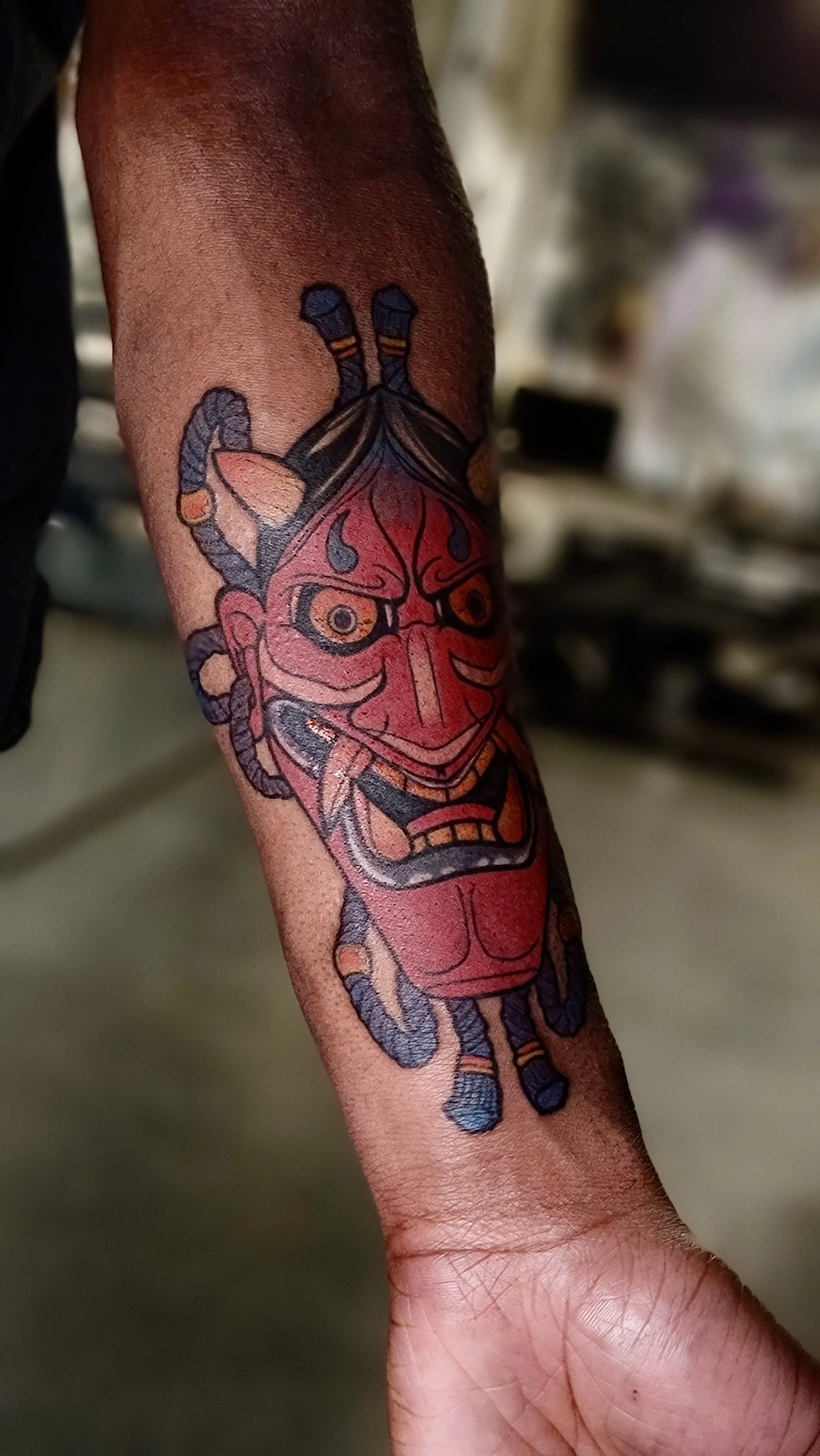 Colorful tattoo of a traditional Japanese Hannya mask on a person's forearm.