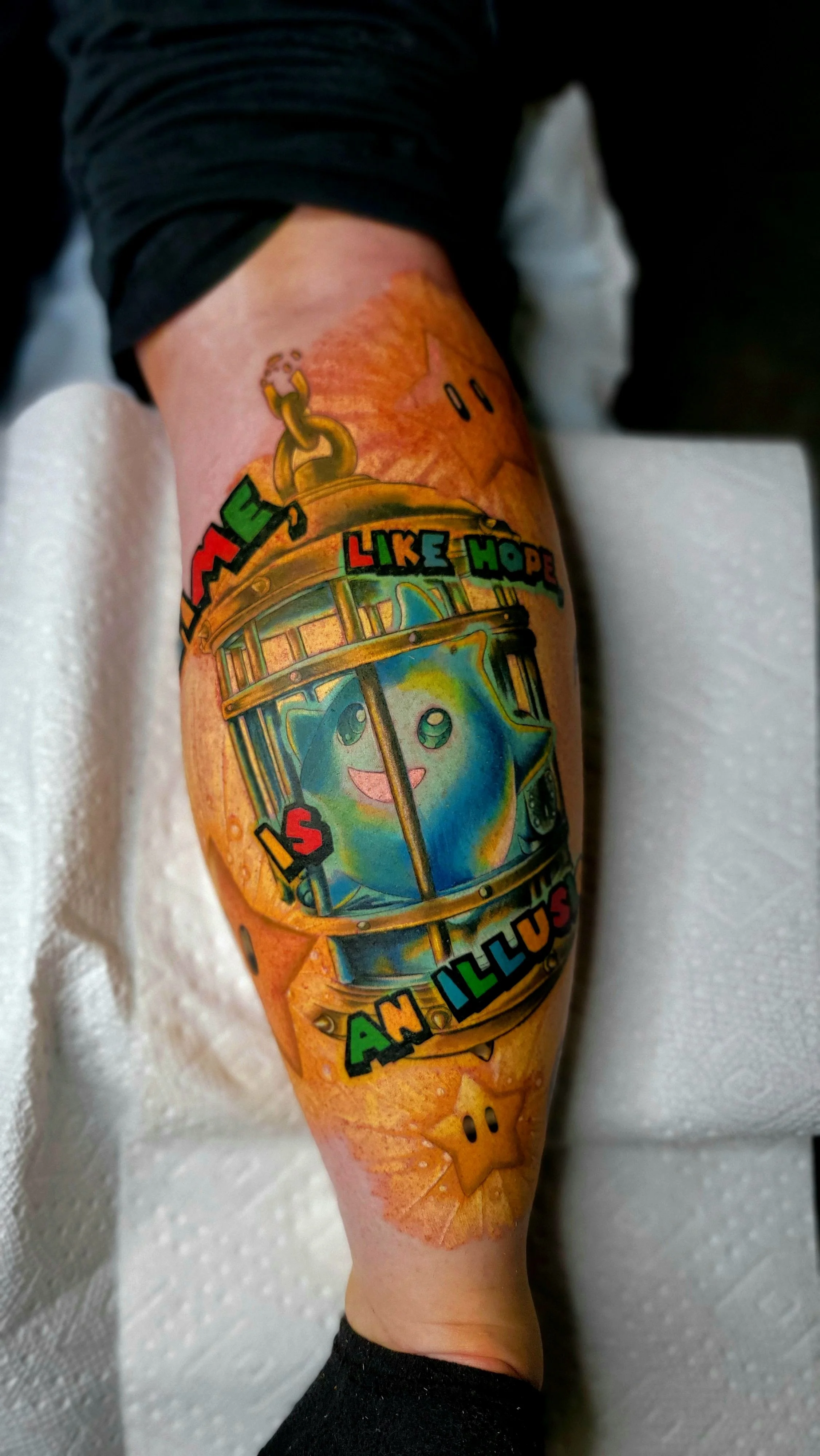 Colorful tattoo of a smiling cartoon character with rainbow colors on the arm, with text around it in bright colors, on a person's upper arm.