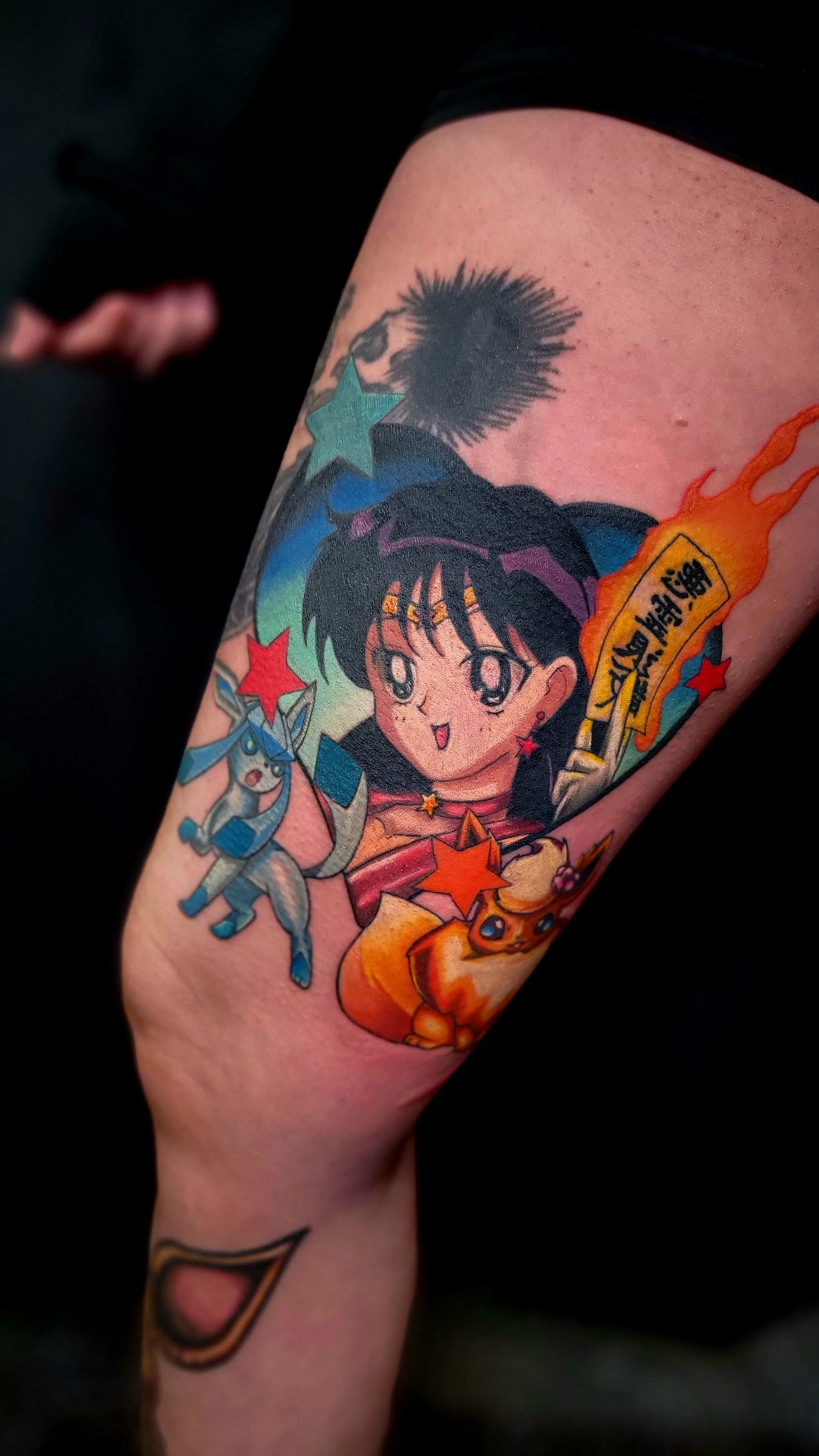 Colorful anime-style tattoo on person's arm featuring a young girl with black hair, surrounded by stars, a creature resembling a bunny with a star on its forehead, a fiery Poké Ball, and Japanese characters.