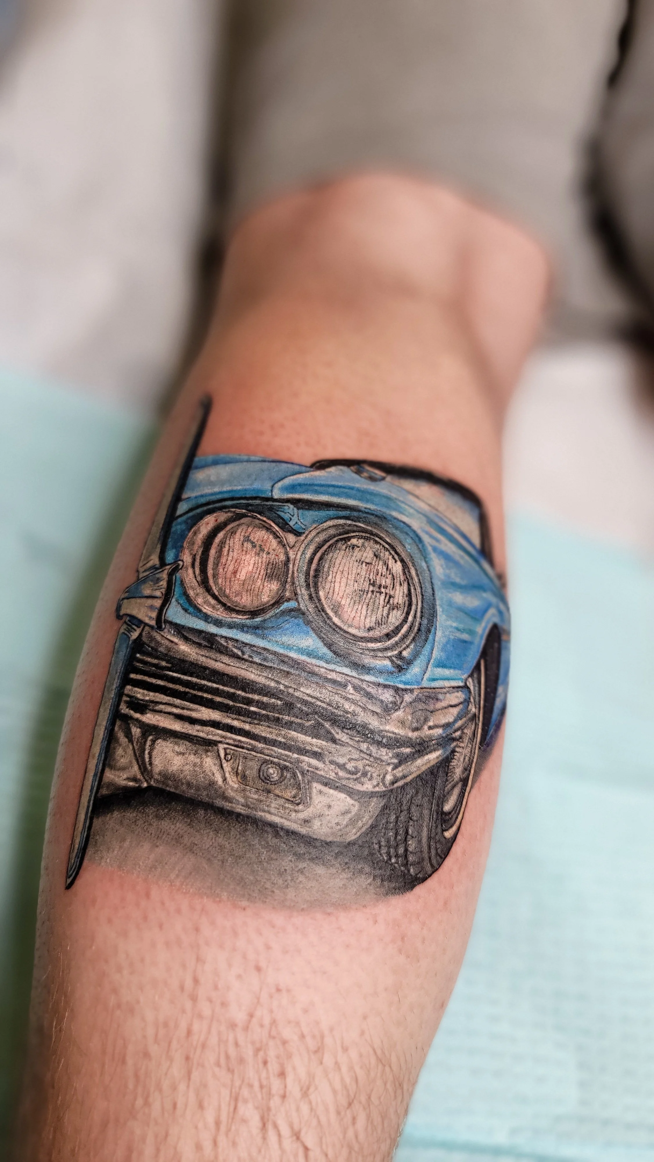 Tattoo of a blue and black classic car on person's forearm.