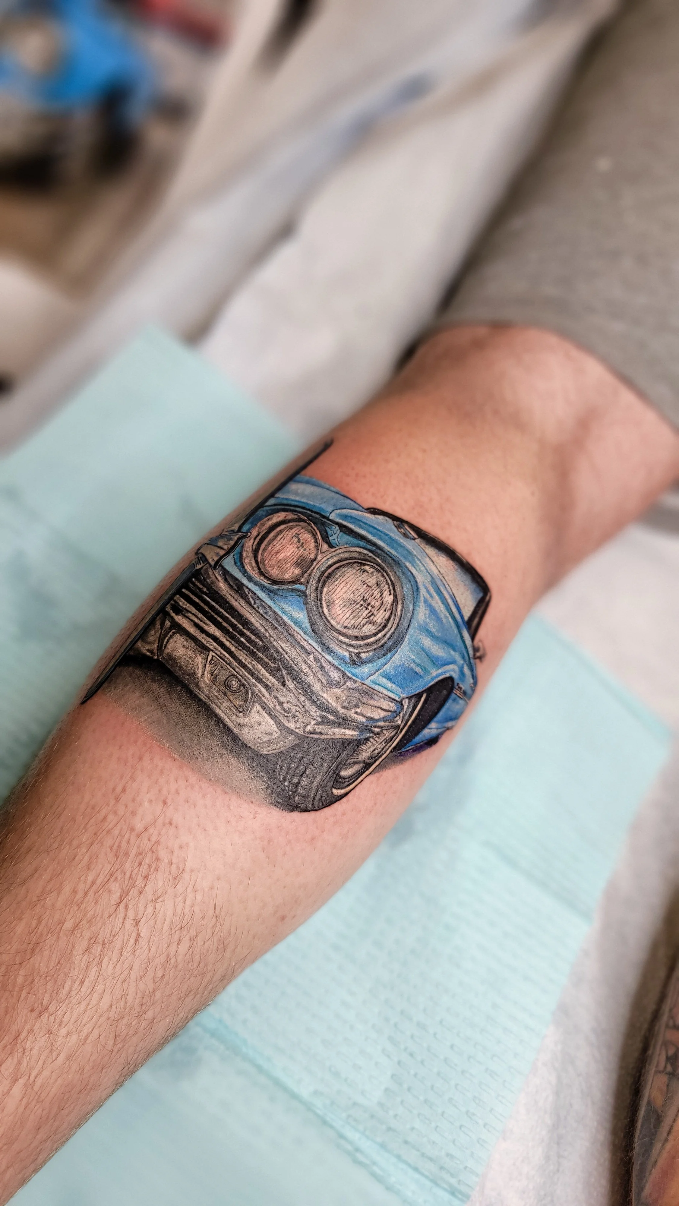 Tattoo of a blue and black sports car on person's forearm.