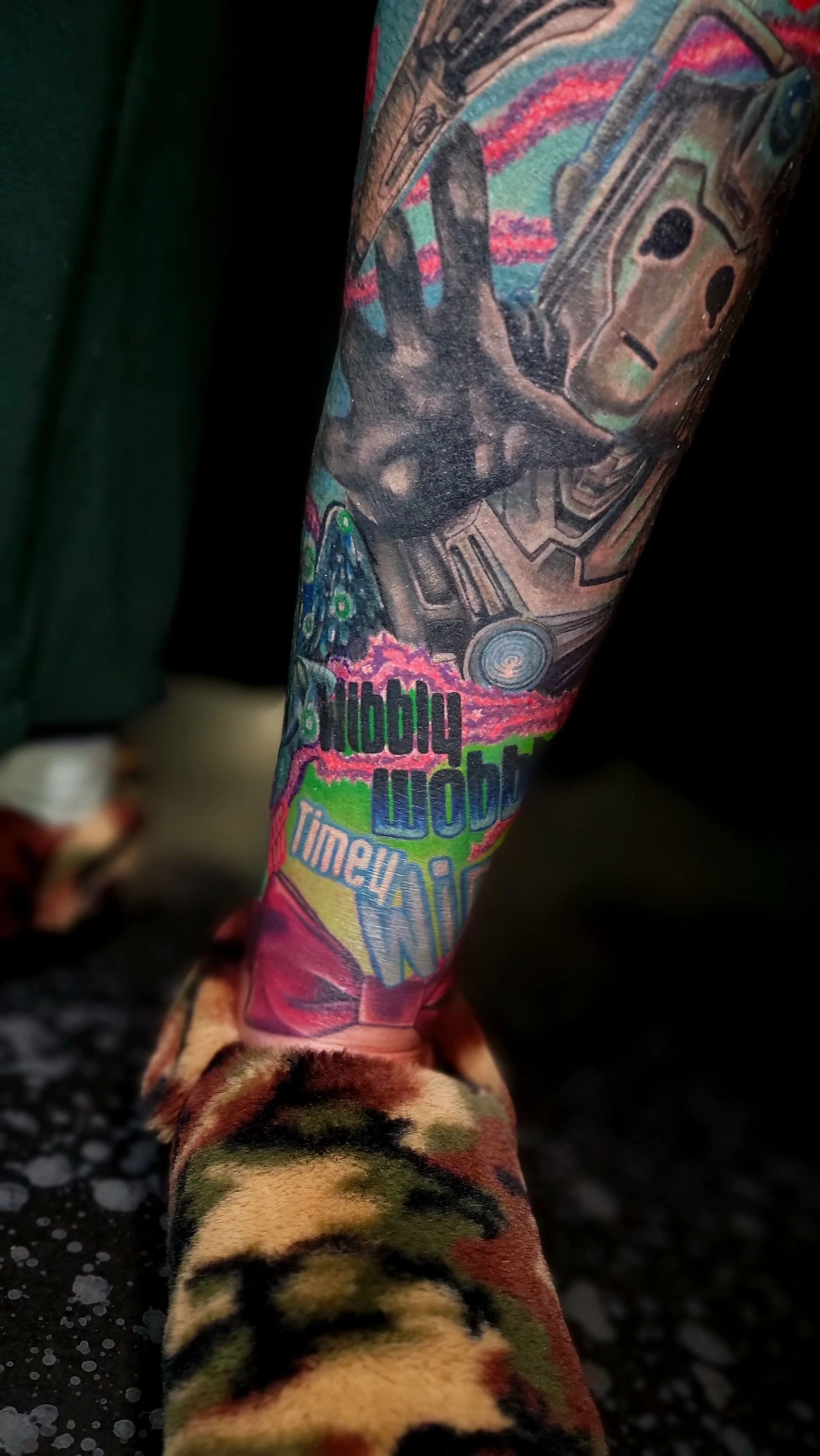 Colorful tattoo sleeve featuring psychedelic patterns, a hand making a peace sign, and vibrant, comic-style text that includes the words "Wobby Wob" and "Time" on a person's arm.