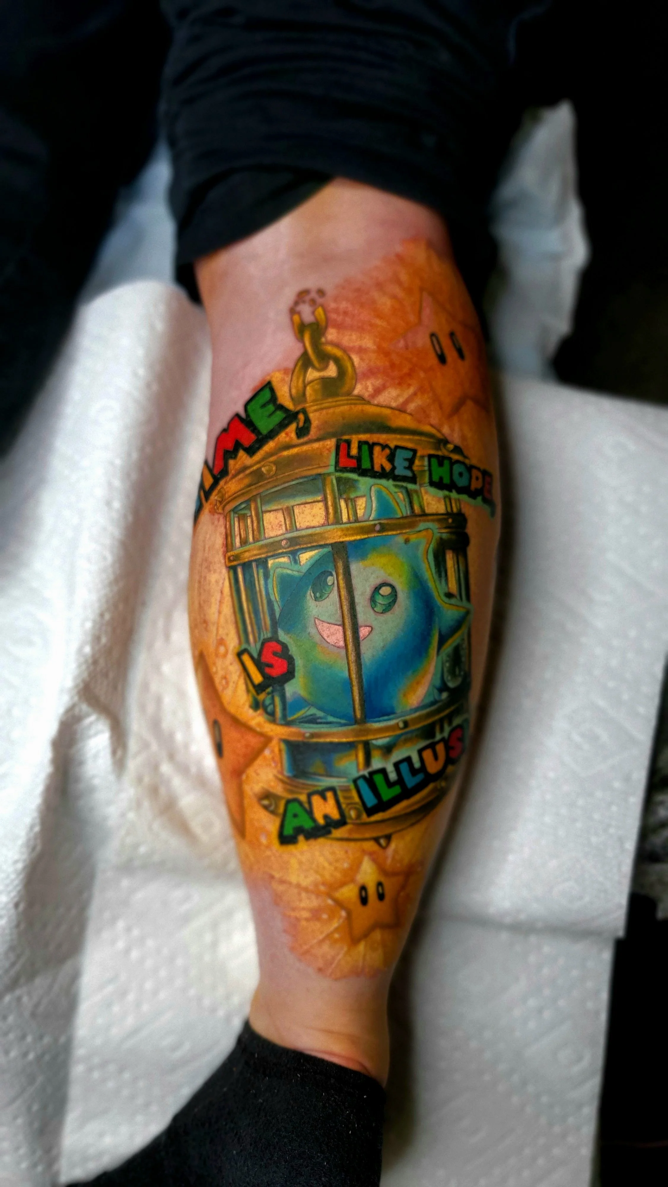 Colorful tattoo on person's forearm featuring a cartoonish star character with a happy face, a gold chain, and the text "LIKE HOPE" and "AN ILLUSTRATOR".
