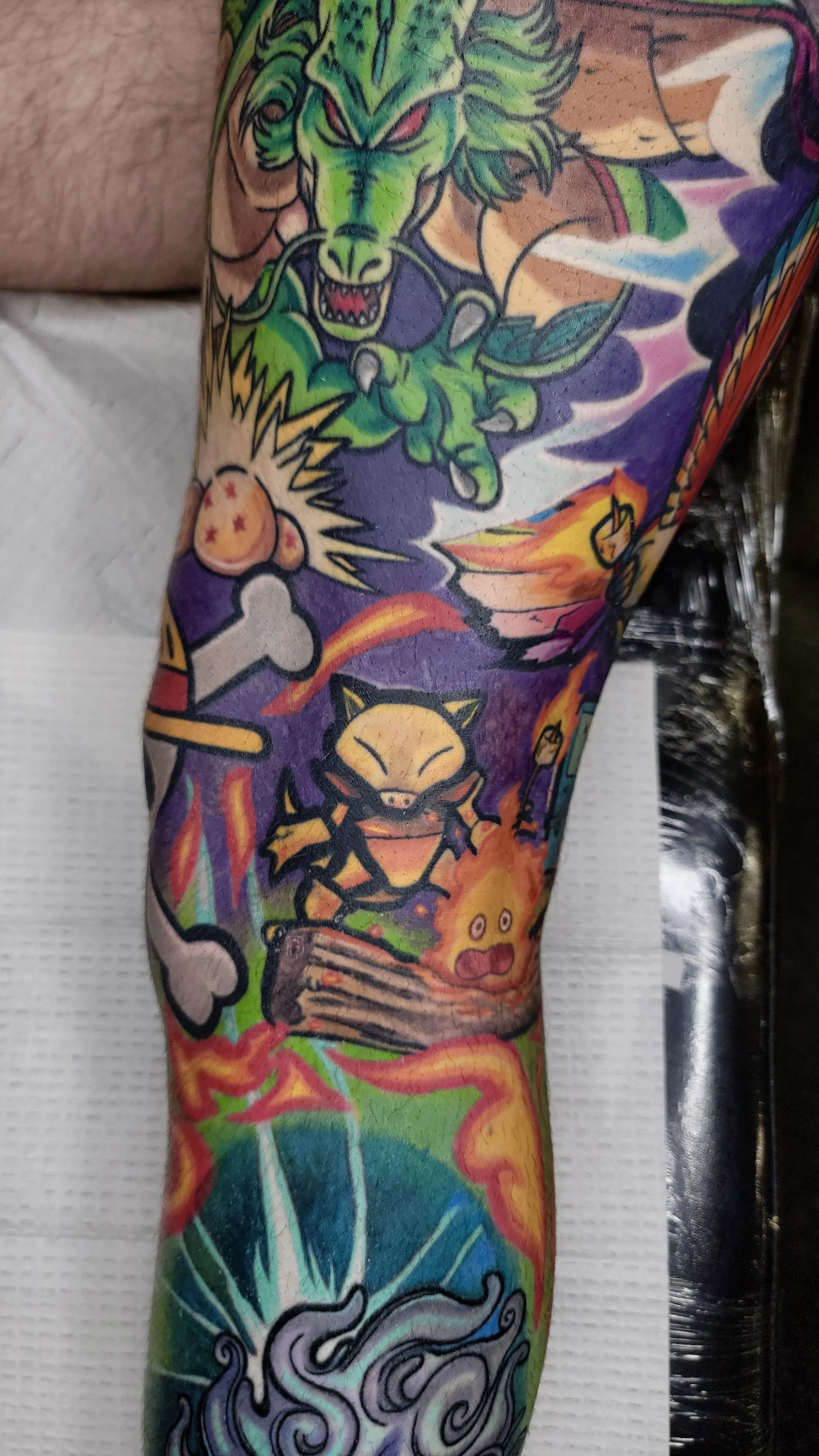 Colorful tattoo sleeve featuring a green dragon, a cartoonish rabbit, a yellow cat, a flying pig, and various abstract and fantasy elements.