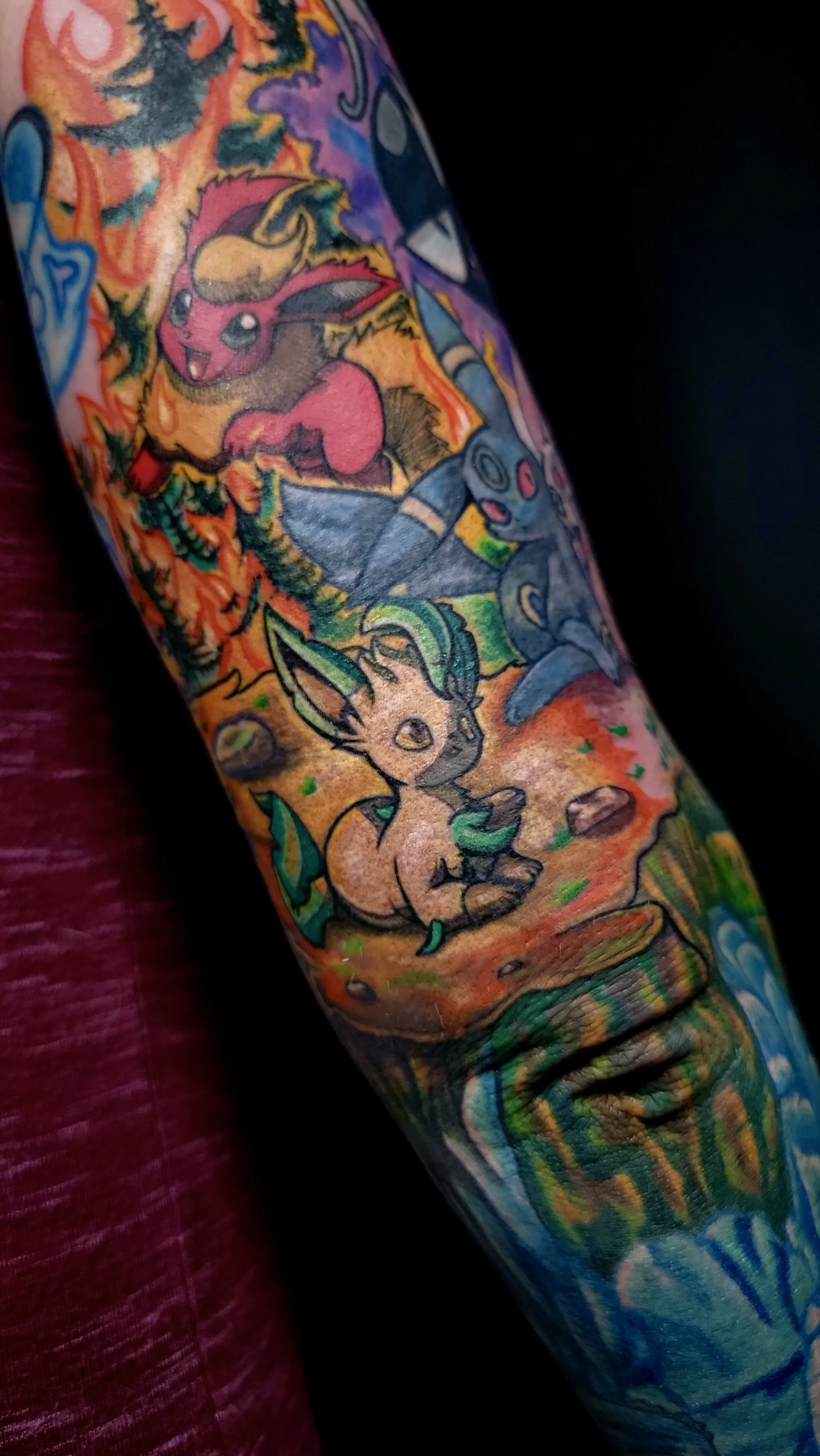 Colorful tattoo sleeve featuring cartoon Pokémon characters, including Eevee, Pikachu, and Umbreon, with vibrant background imagery.