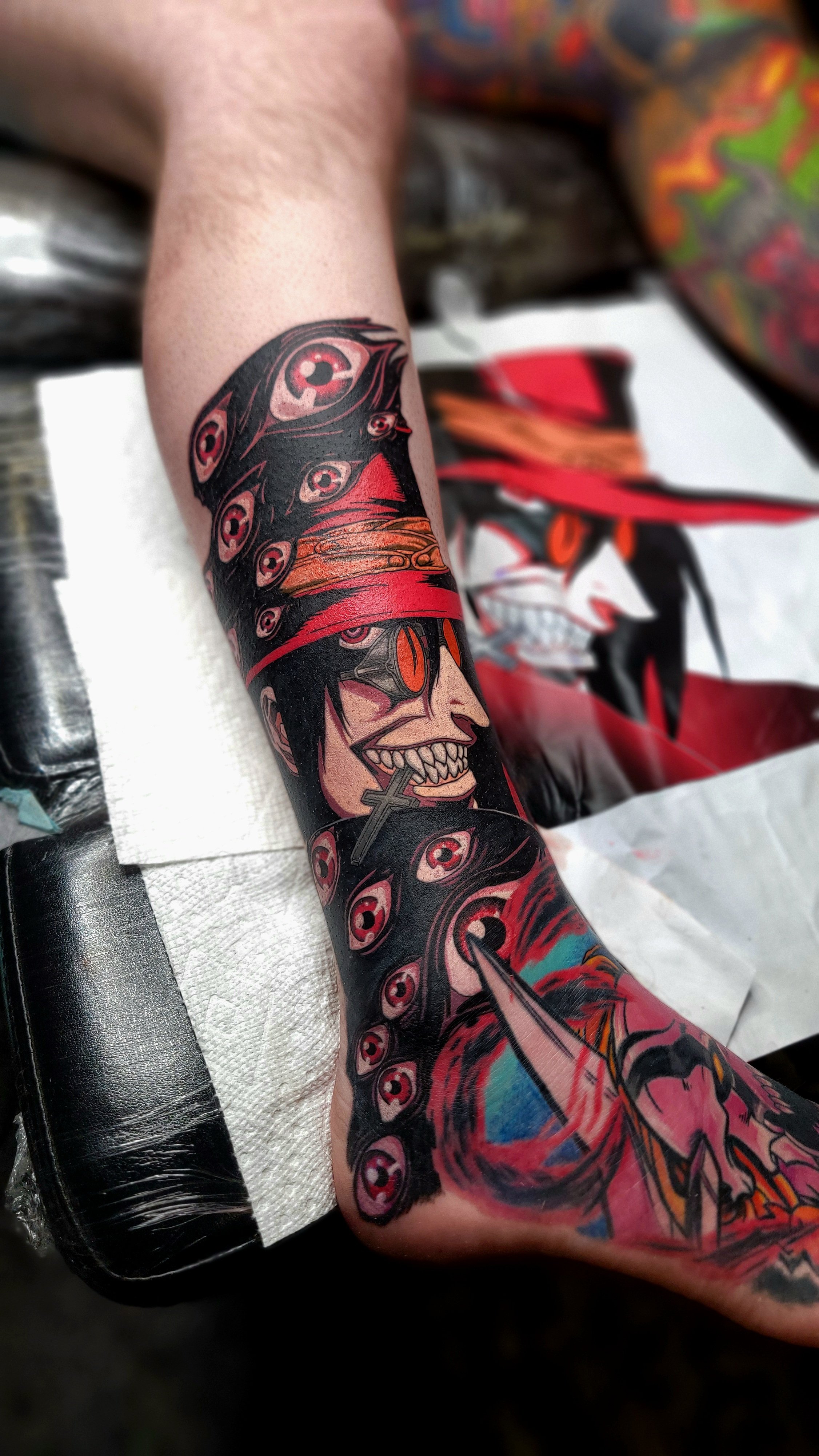Colorful tattoo of a grinning skeleton wearing a red hat and sunglasses, with a snake coiled around its neck, on a person's arm.