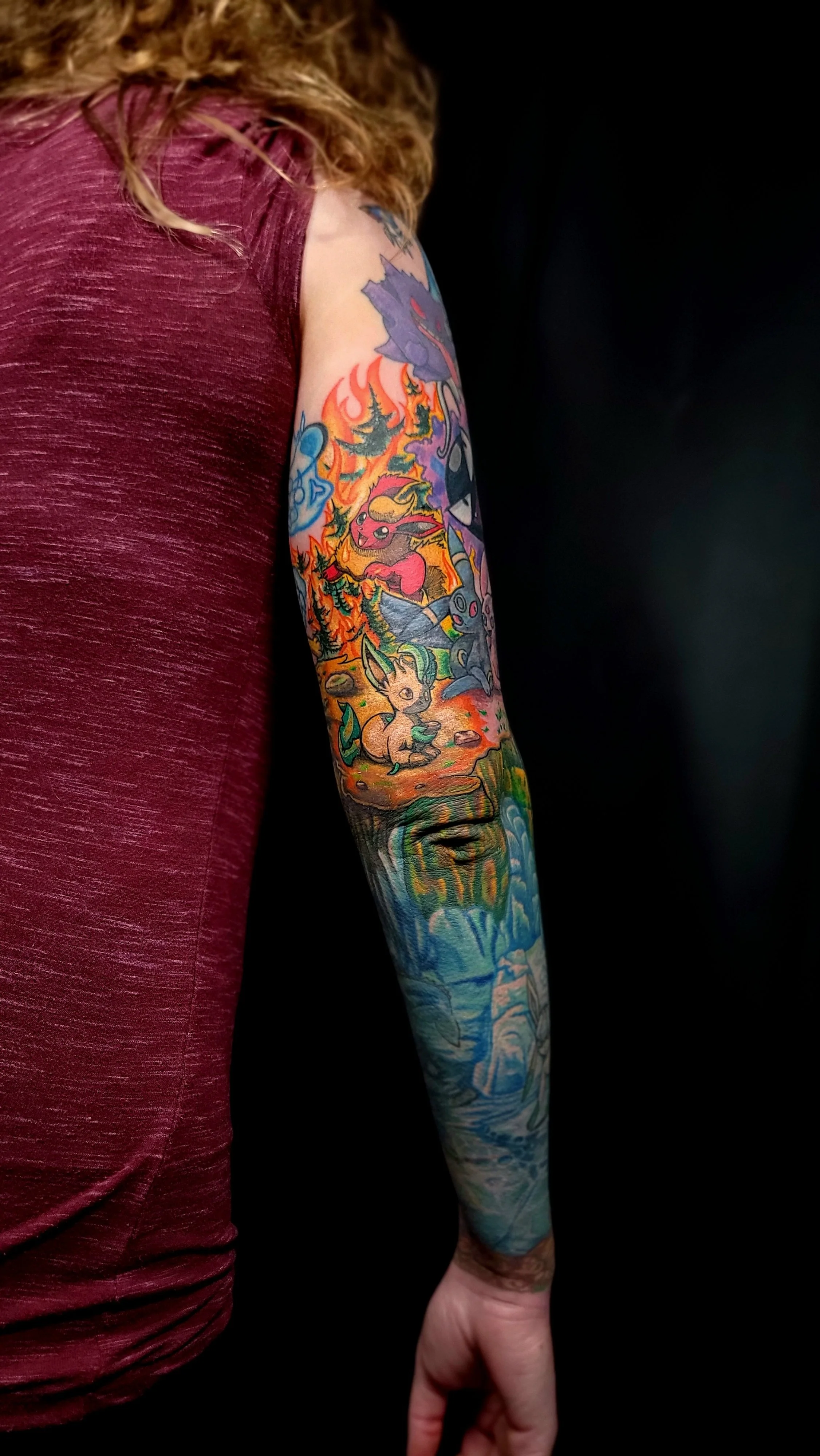 Colorful tattoo sleeve featuring various Pokémon characters and a scenic background on a person's arm.