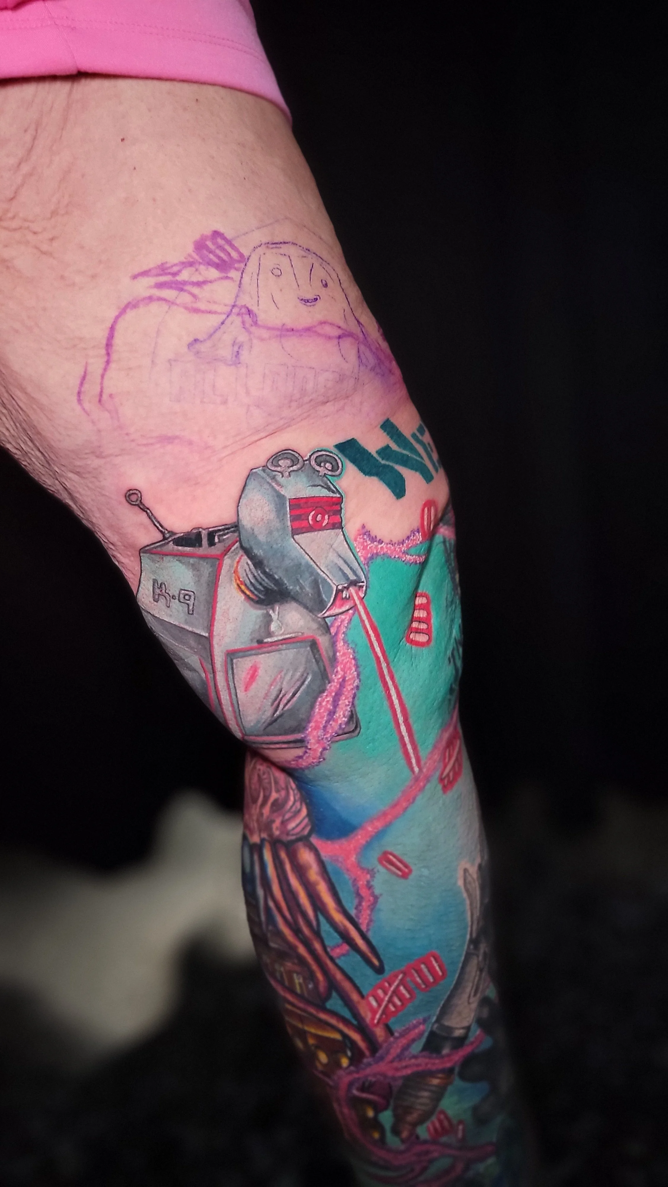 Colorful tattoo sleeve featuring a ray gun, abstract designs, and a cartoonish face on the upper arm.