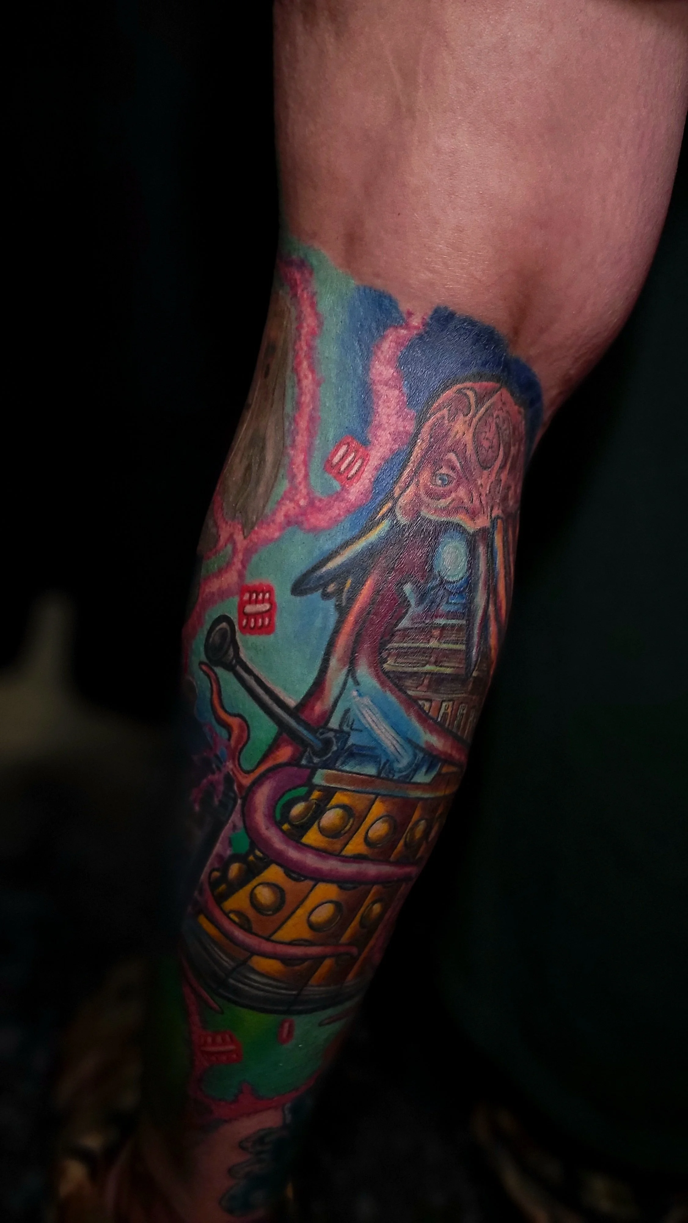 A colorful tattoo on a person's arm featuring abstract and surreal elements, including shapes, vibrant colors, and detailed designs.