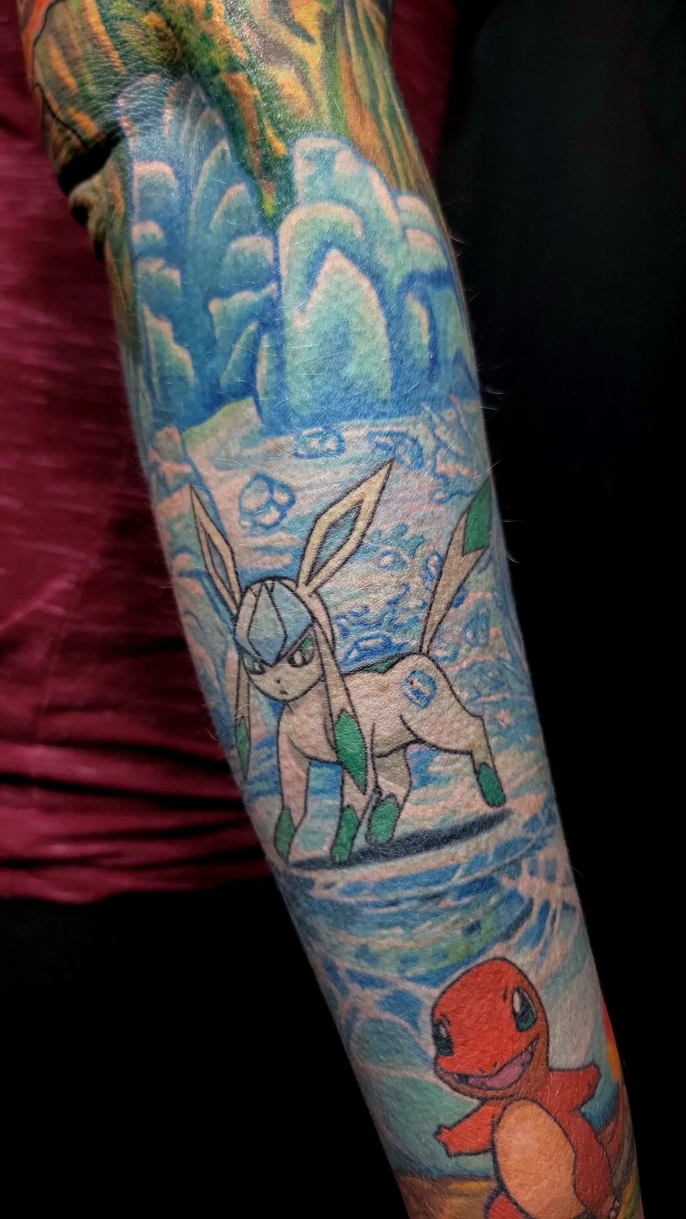Colorful tattoo sleeve featuring a cartoon of Eevee and Charmander, Pokémon characters, with dynamic background patterns.