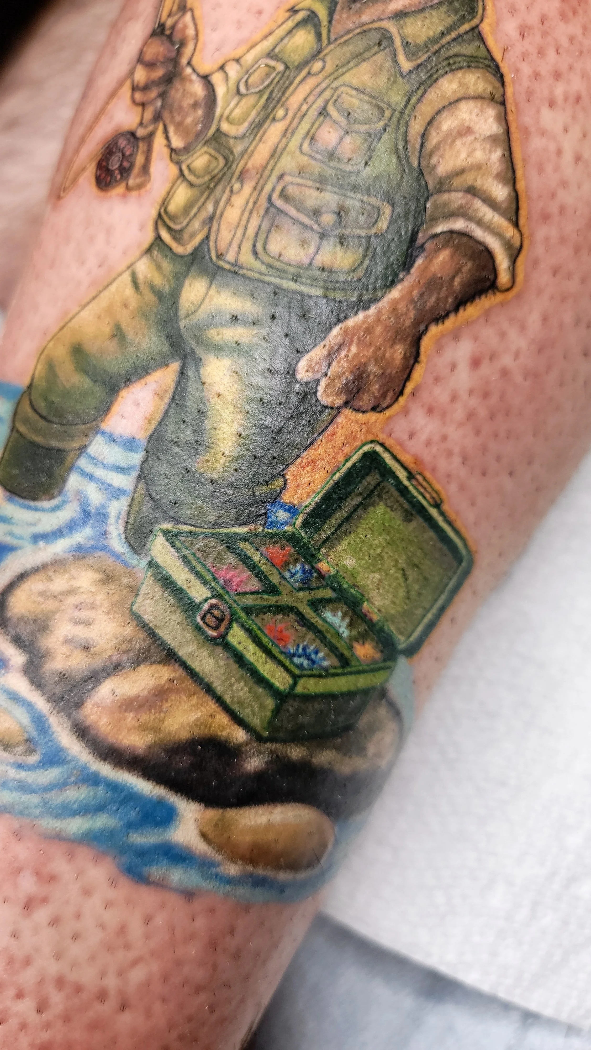Tattoo of a soldier holding a gun and looking at a treasure chest filled with jewels.
