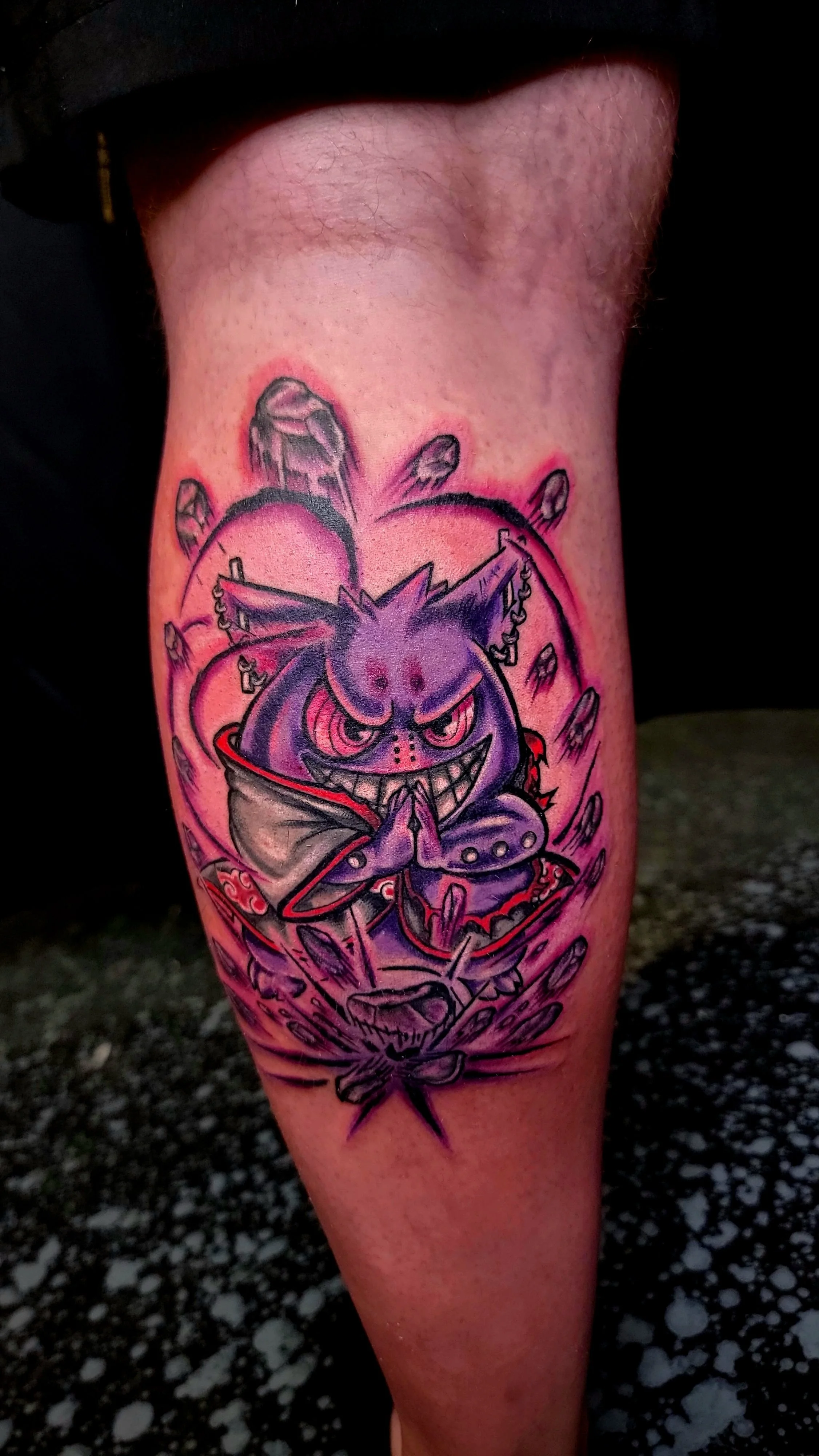 Colorful tattoo of a purple, grinning cartoon character with spiky hair, horns, and a mischievous expression, surrounded by rocks and bats, on a person's upper leg.