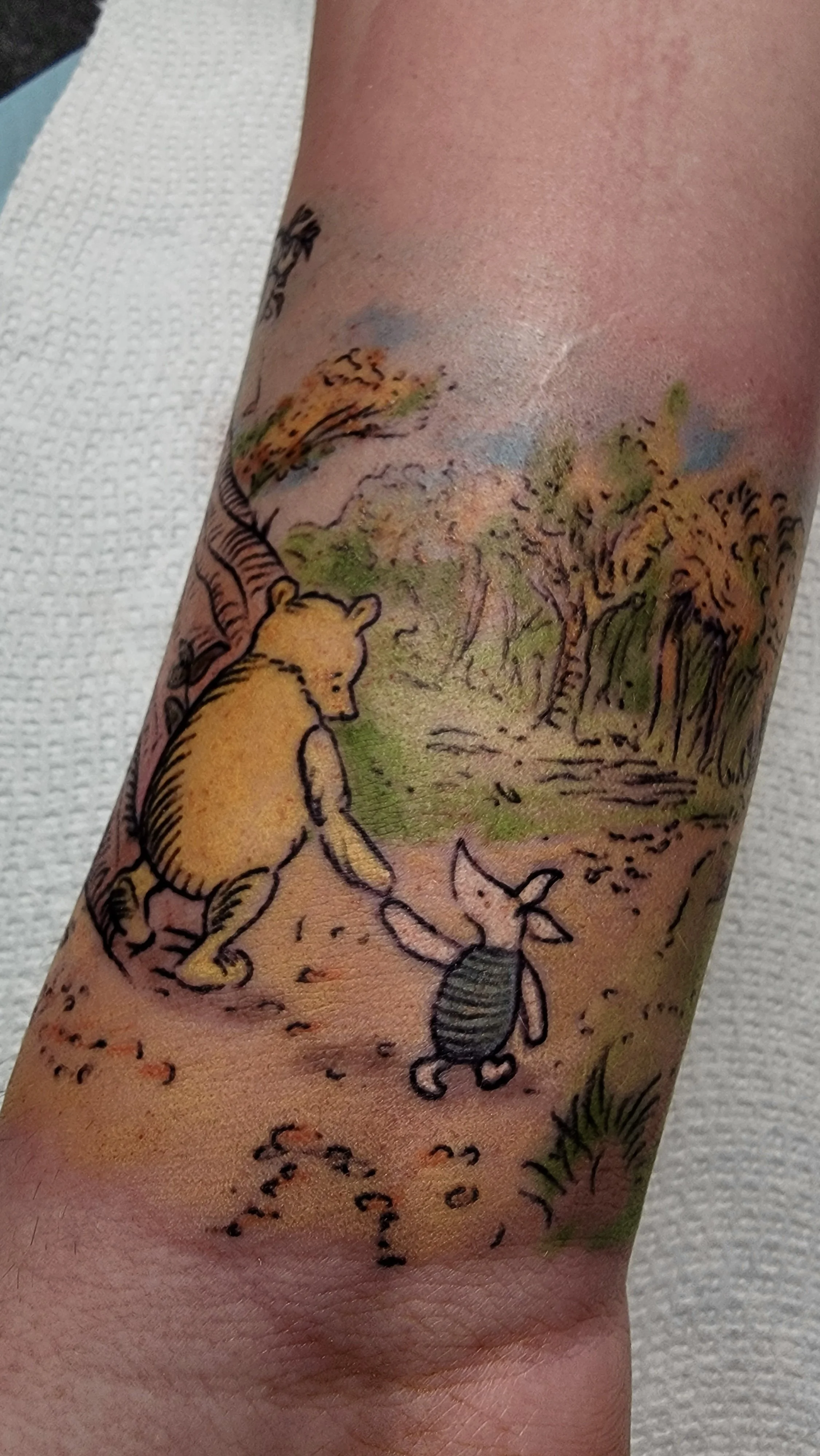 Tattoo on arm depicting a bear cub sitting on the ground, a fox leaping in the background, and a large insect crawling on the ground amidst trees and foliage.