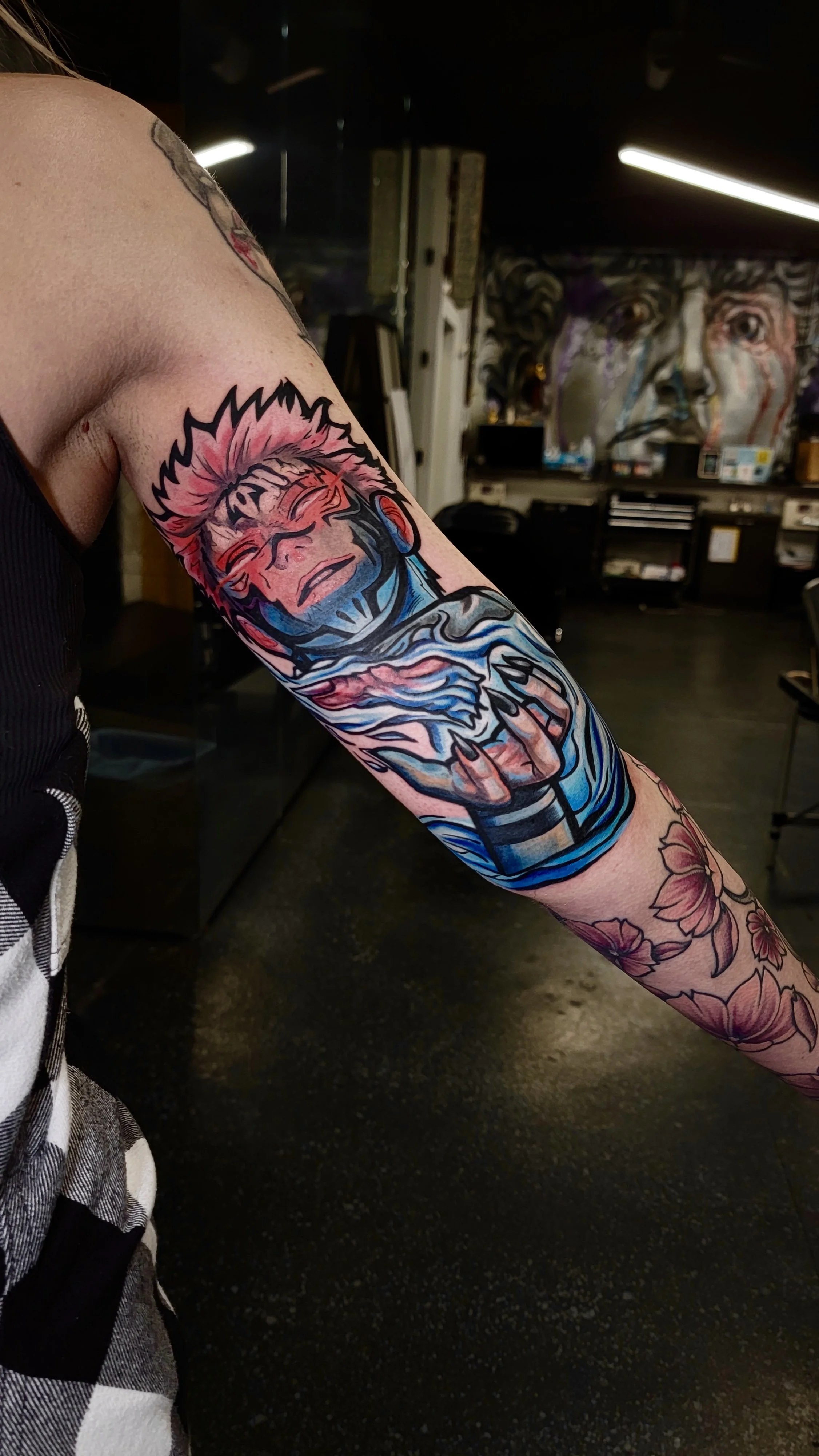 Colorful tattoo of a smiling face with spiky hair and a hand holding a cup, featuring floral designs on the wrist.